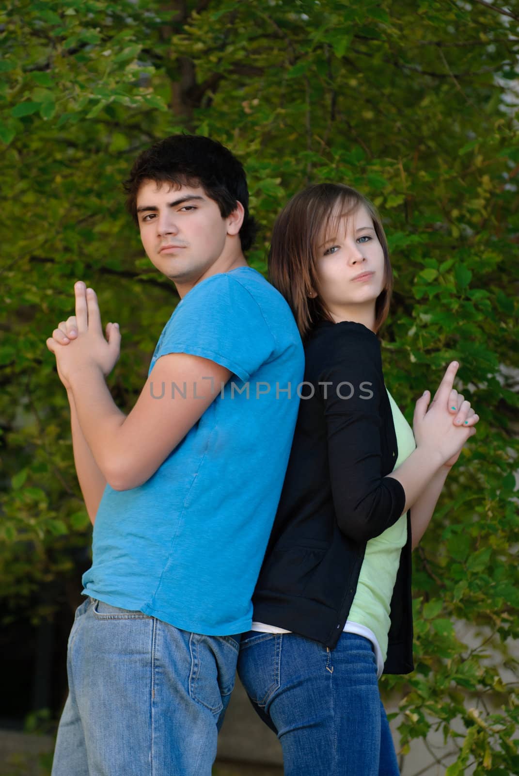 Two teens having fun and pretending to hold guns while standing back to back.