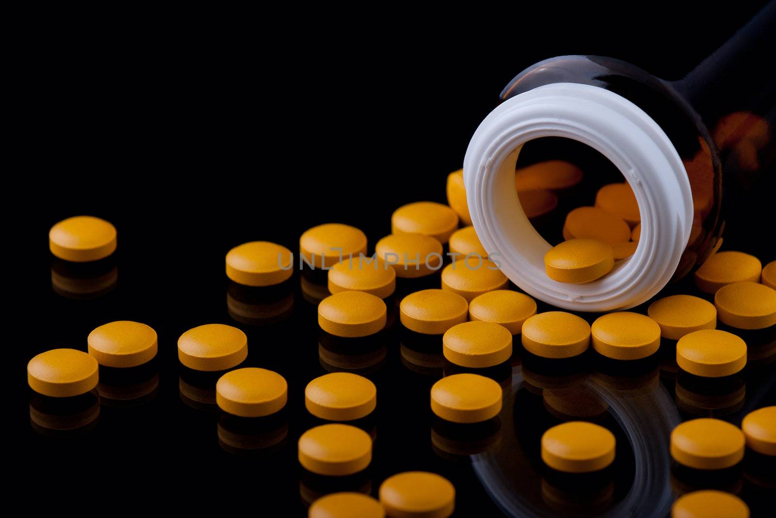 Yellow Pills and pill bottle on mirroring surface