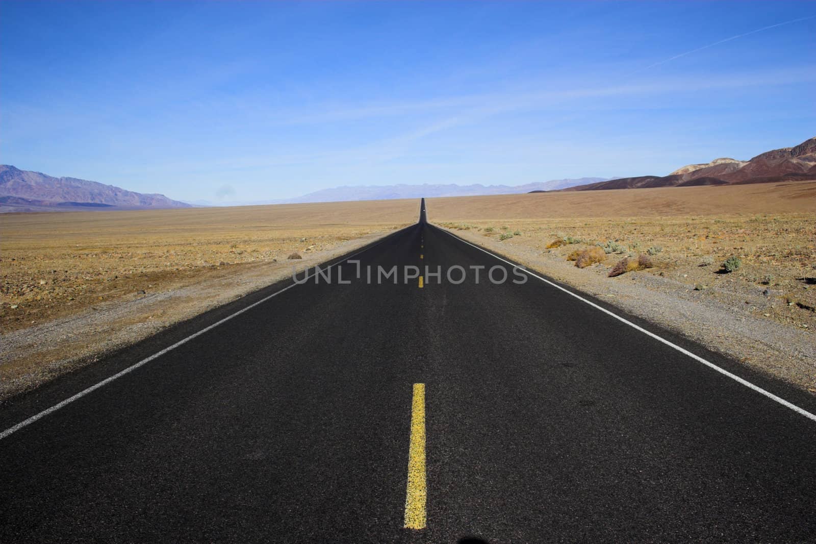 Desert road going through mineral deposits and geological formations of Death Valley National Park