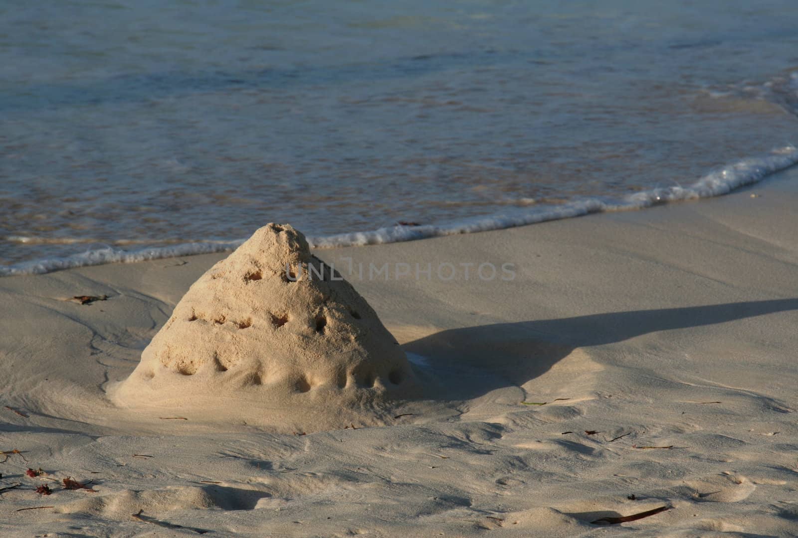 A sand castle slowly being washed away by the tide.