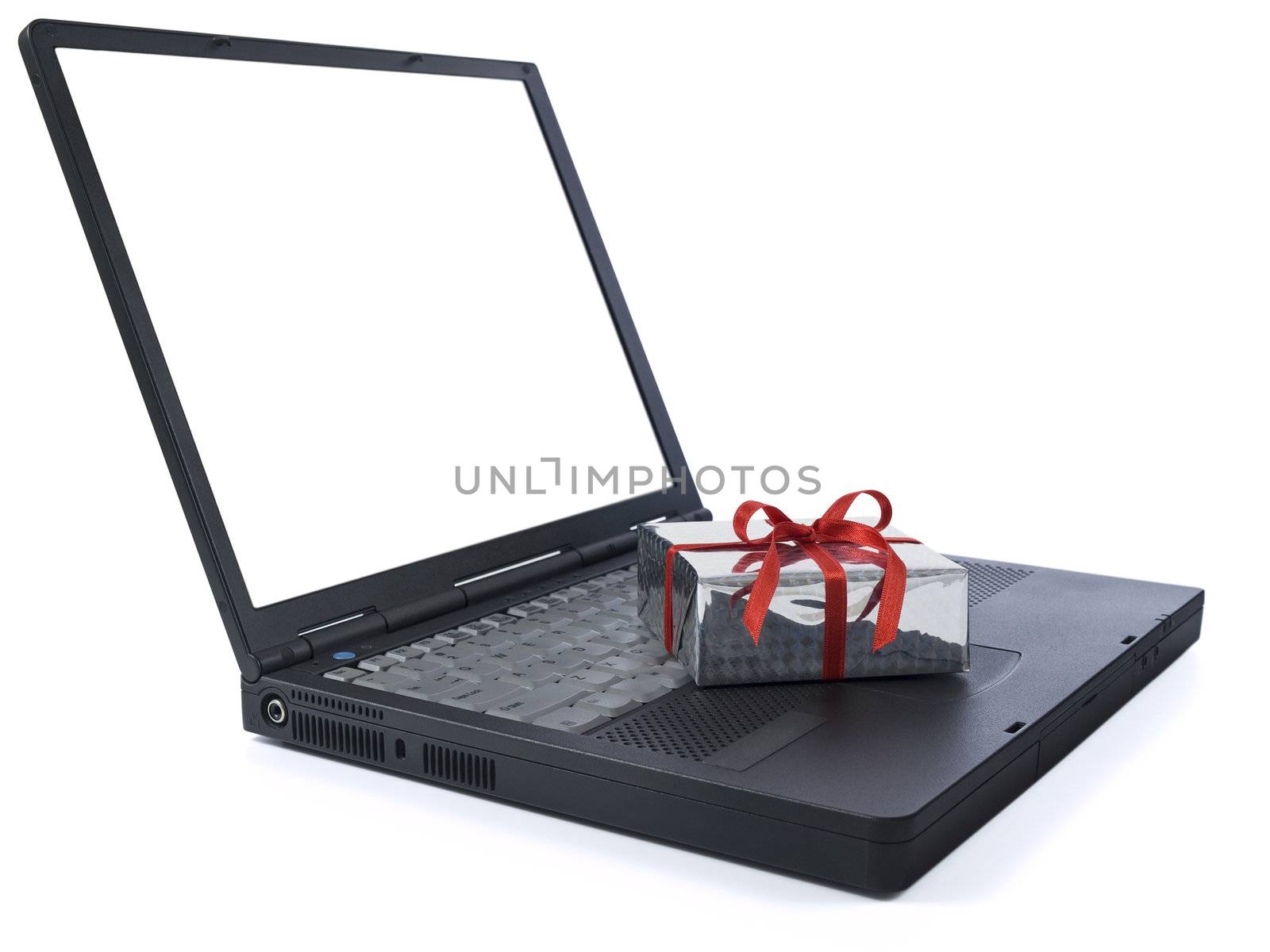 Small gift wrapped with a red ribbon over a black laptop isolated on white. White copy space on screen.