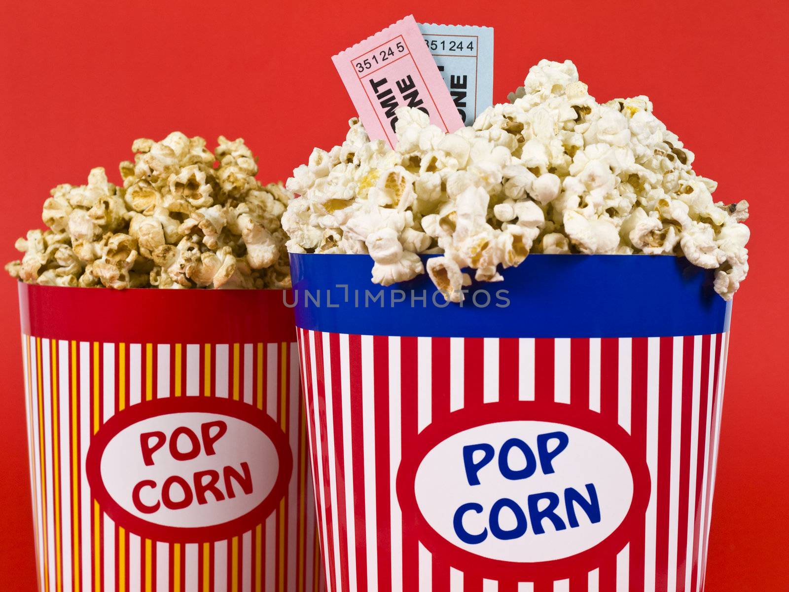 Two popcorn buckets over a red background. Movie stubs sitting over the popcorn.