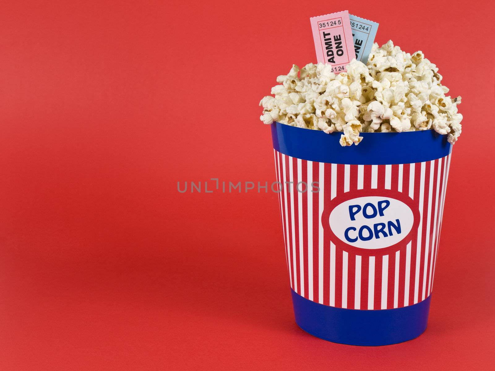 A popcorn bucket over a red background. Movie stubs sitting over the popcorn.