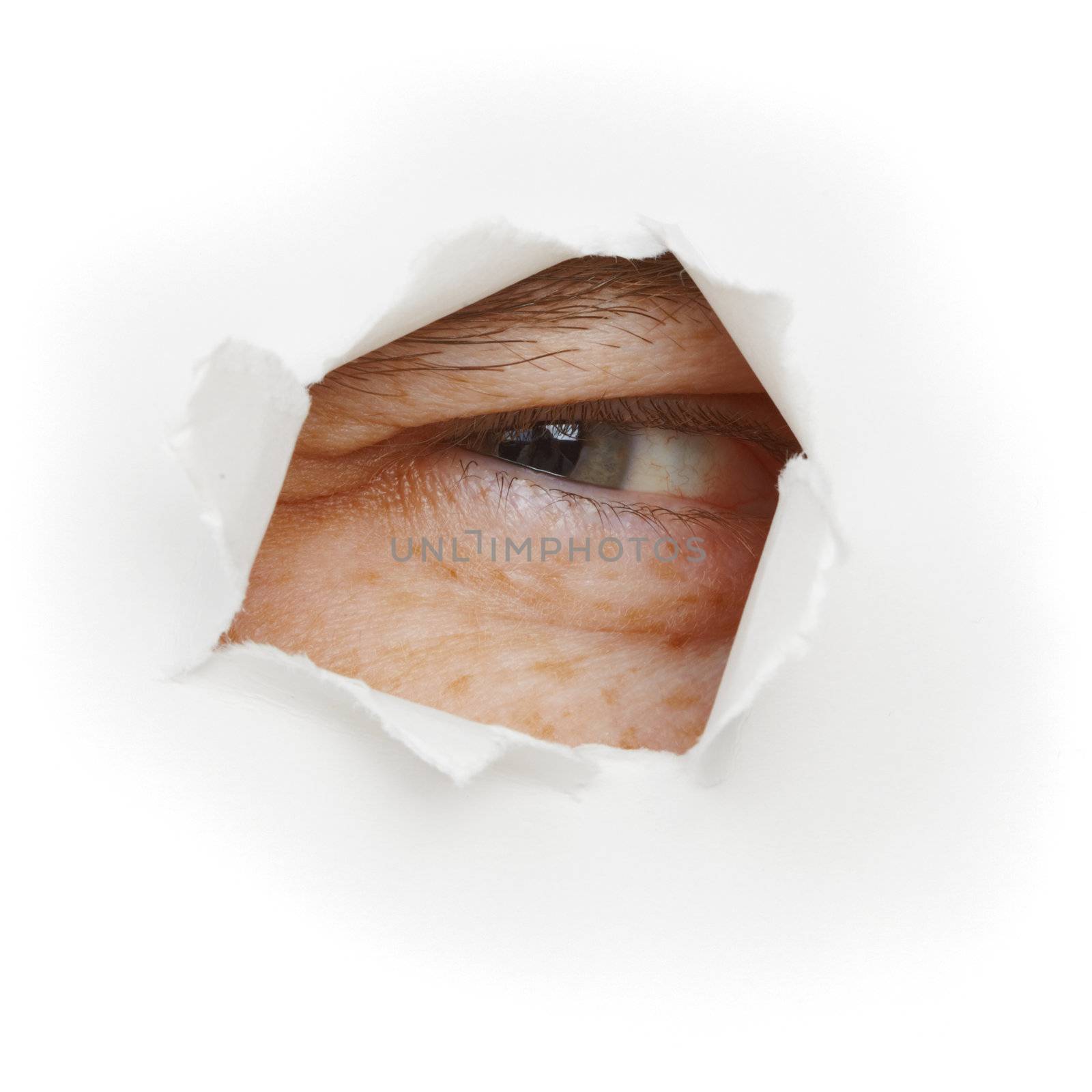 Squinting eye looks through a hole in white paper