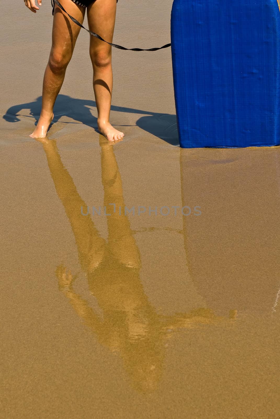 Young girl standing on the beach with reflection in the water on the sand