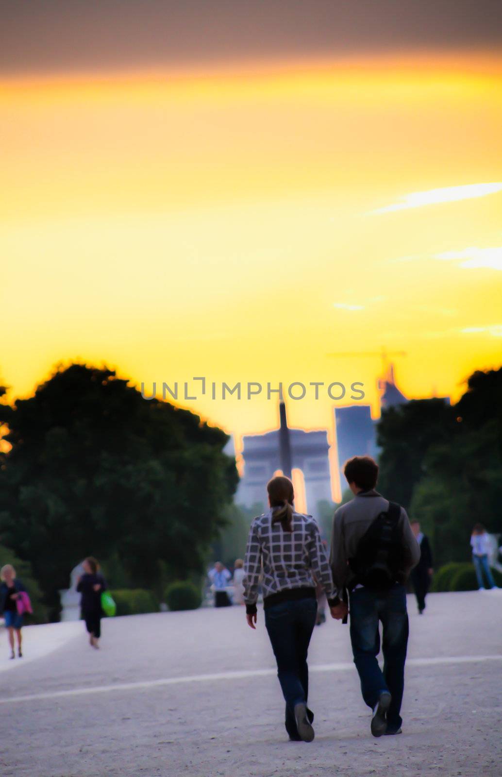 A lovely couple holding hands in sunset, while walking in the direction to Arc de Triomphe. Soft Focus like.
