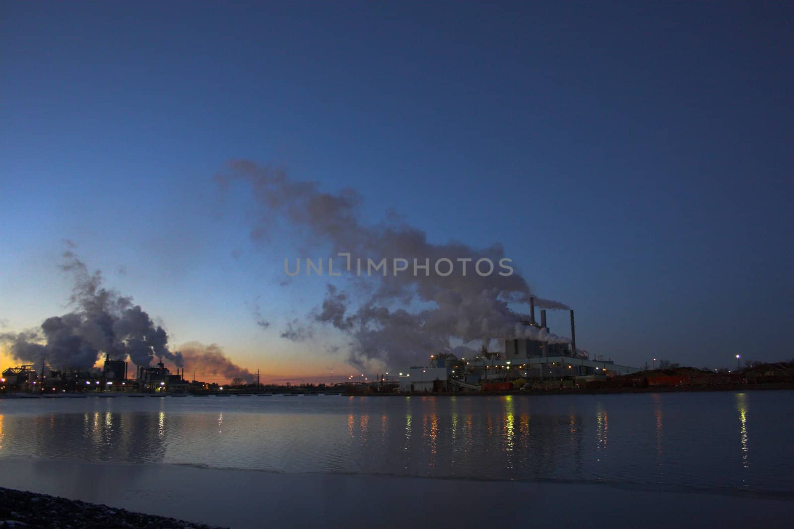 Factory over the river with smoke coming out of the chimneys