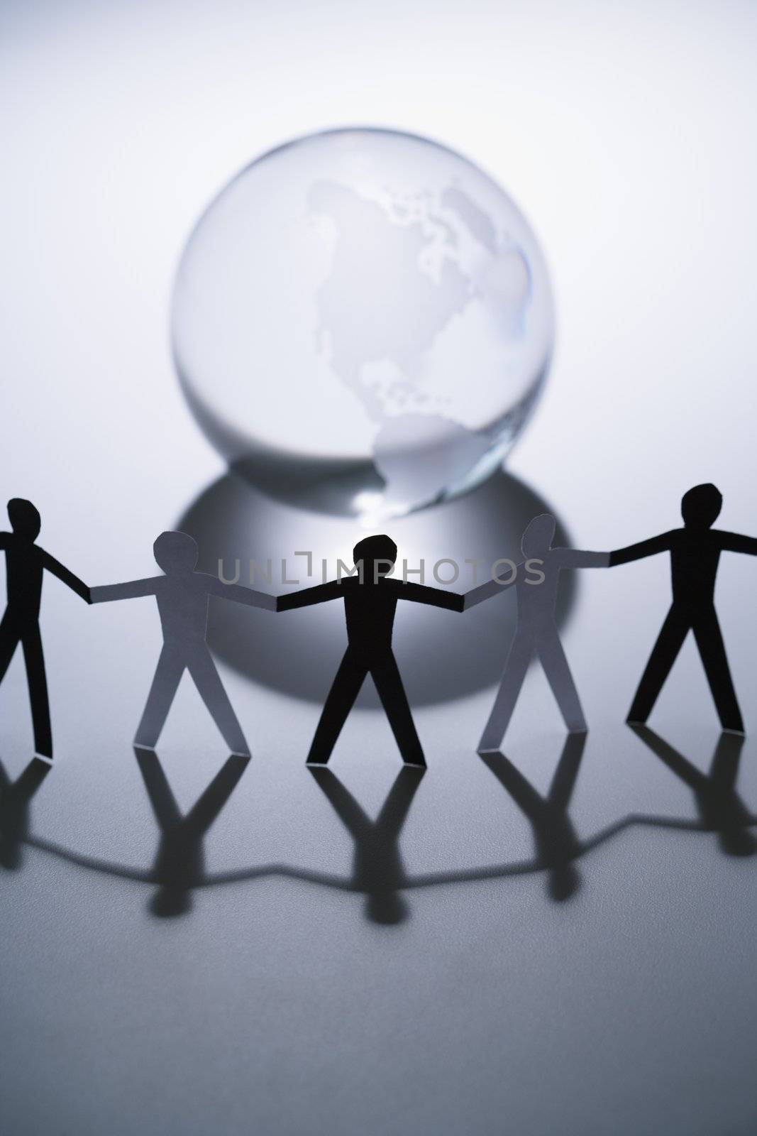 Black and white cutout paper people standing aroung Earth globe holding hands.