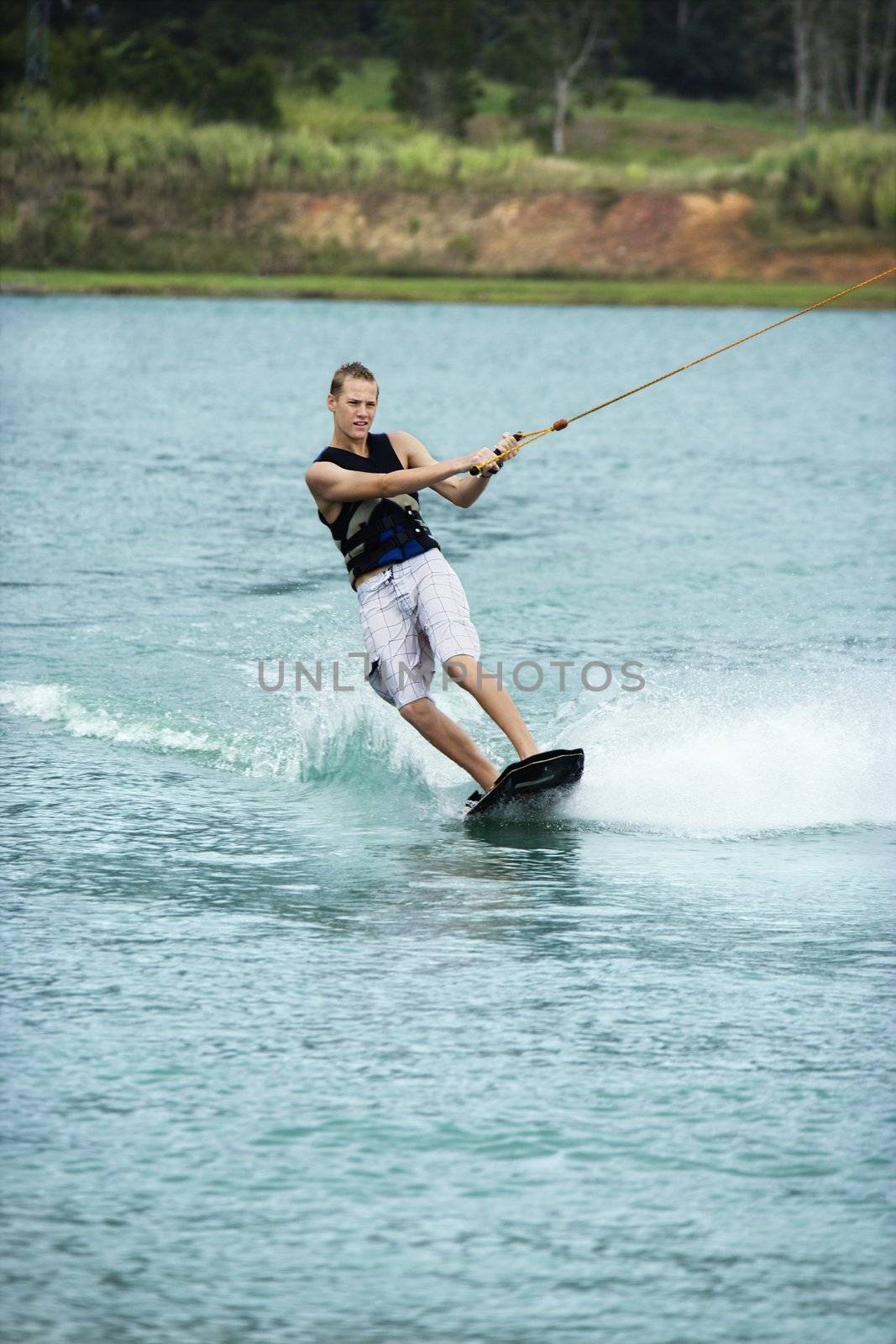 Caucasian young adult male wakeboarding on lake.