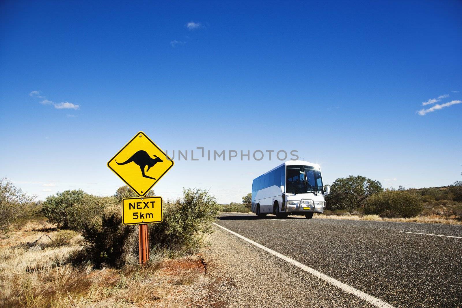 Bus on two lane asphalt road in rural Australia with kangaroo crossing sign.