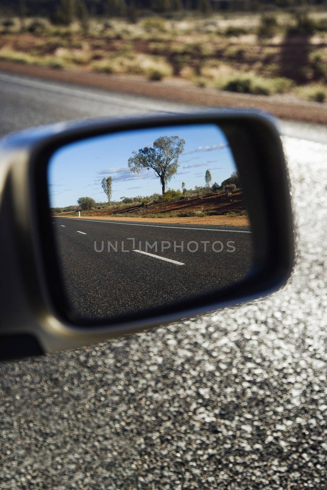 Reflection of rural Australian in rearview mirror of vehicle traveling down two lane asphalt road.