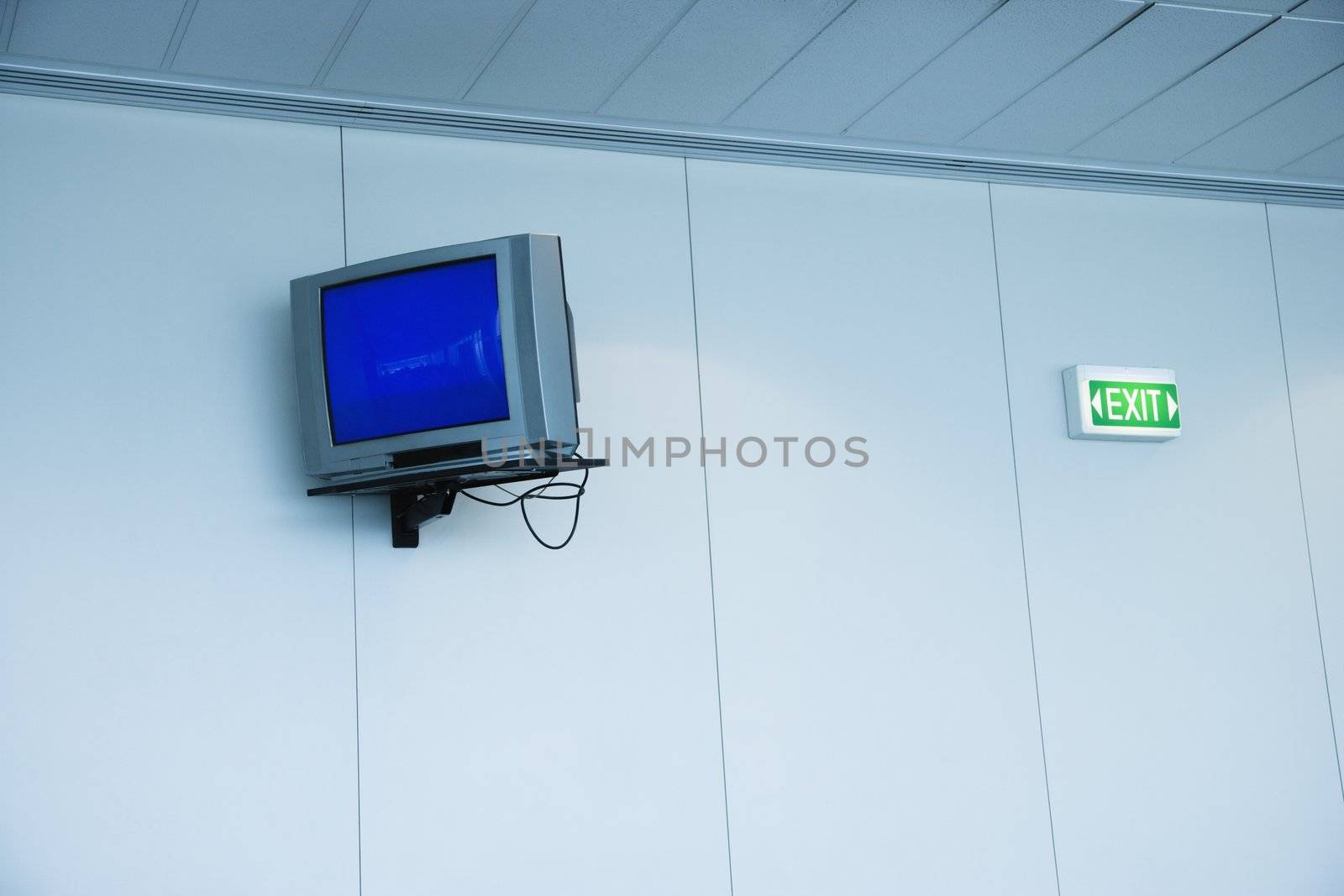 Monitor mounted to wall next to exit sign in airport