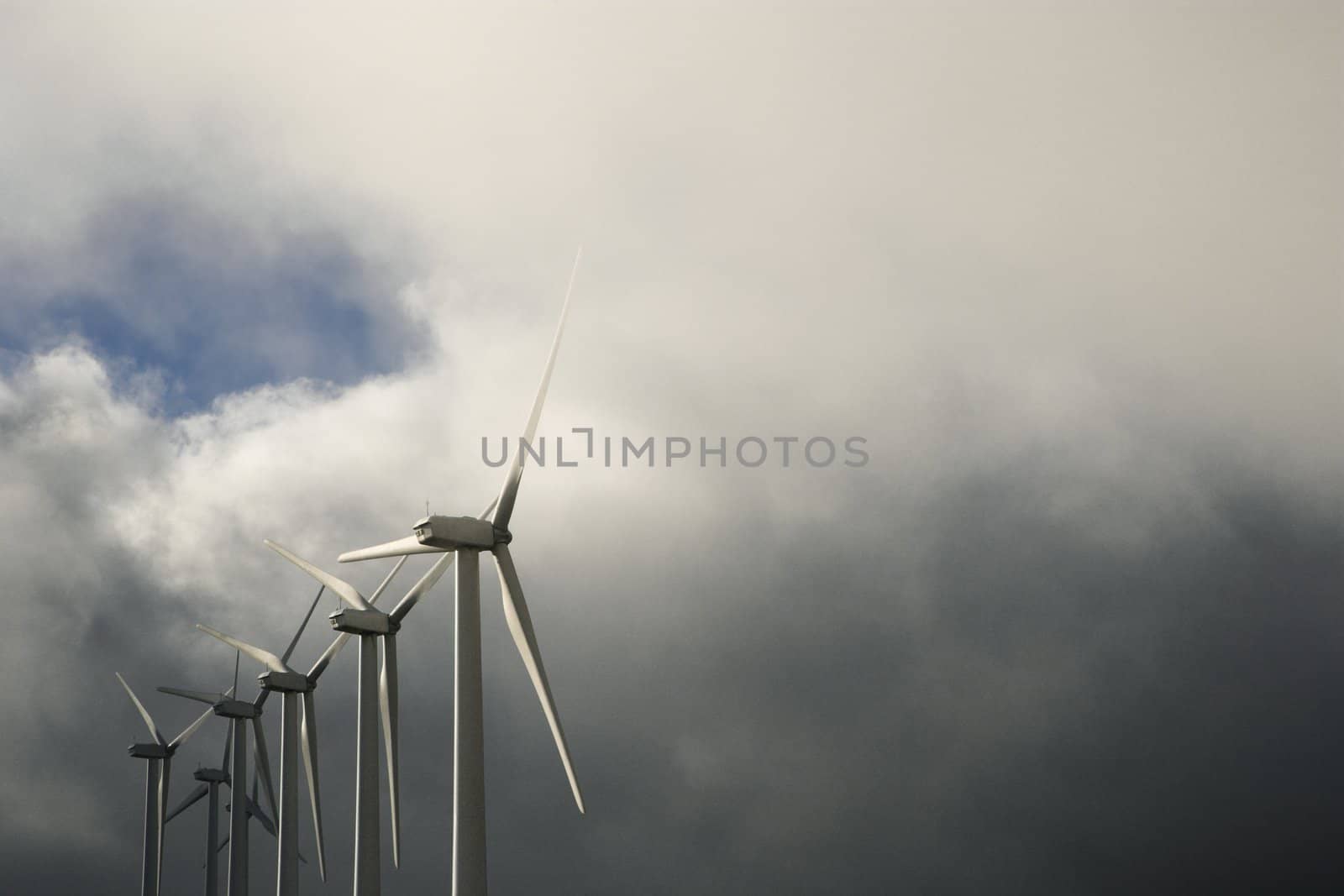 Row of turbines at wind farm again cloudy gray sky.