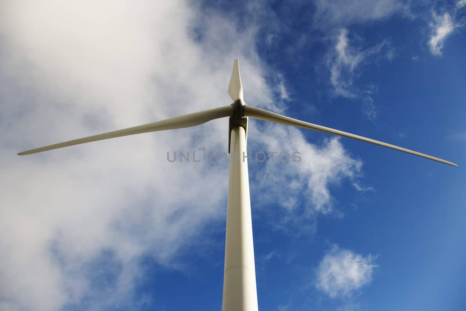 Low angle view of wind turbine against blue sky and clouds.