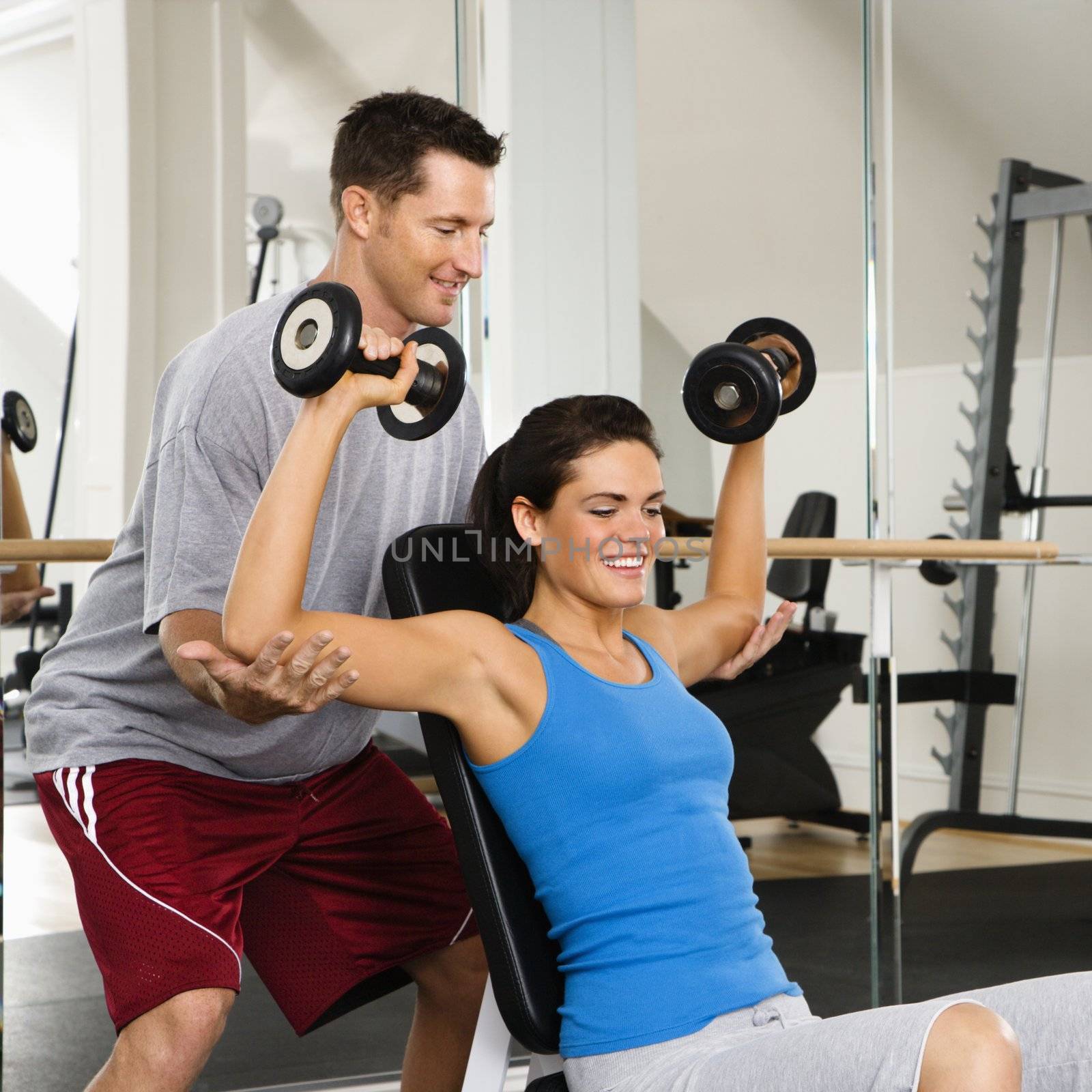 Man assisting woman at gym with hand weights smiling.