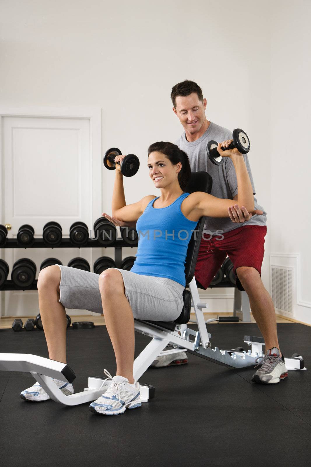 Man assisting woman at gym with hand weights smiling.