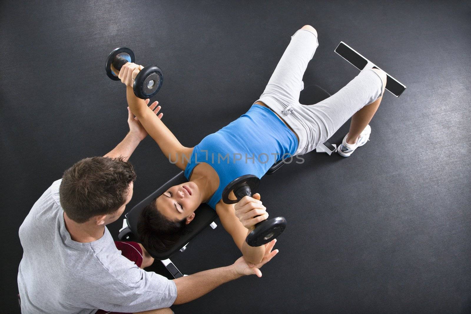 Man assisting woman lifting weights at gym.