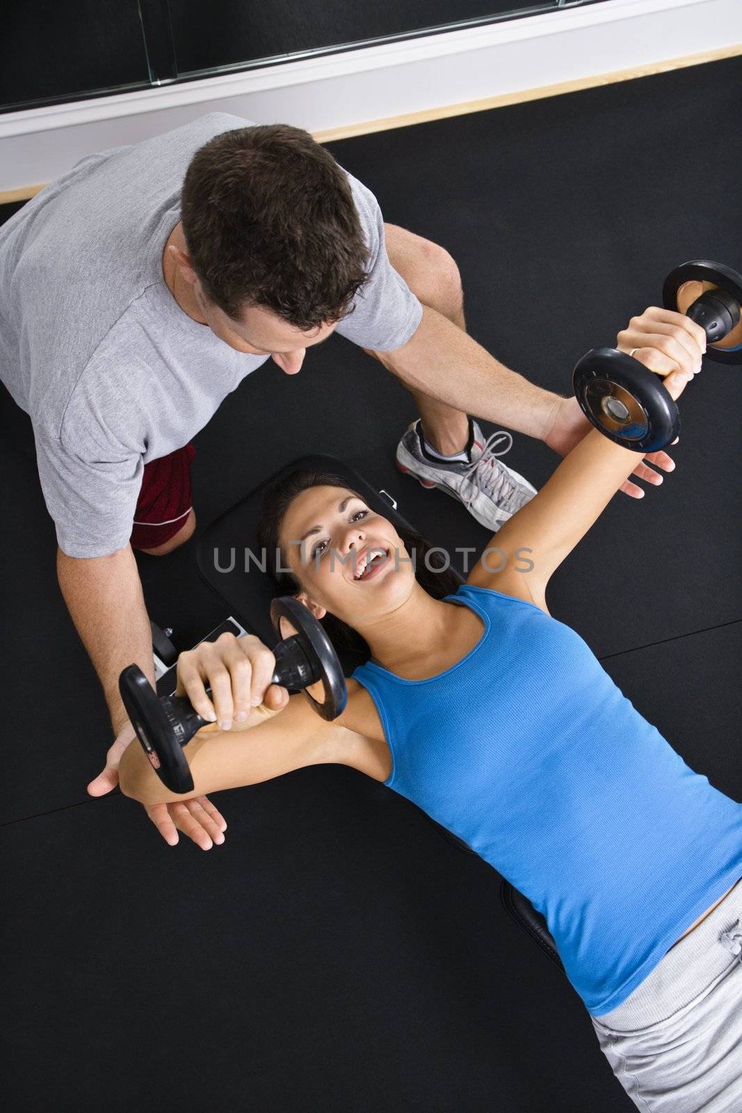Man assisting woman lifting weights at gym.