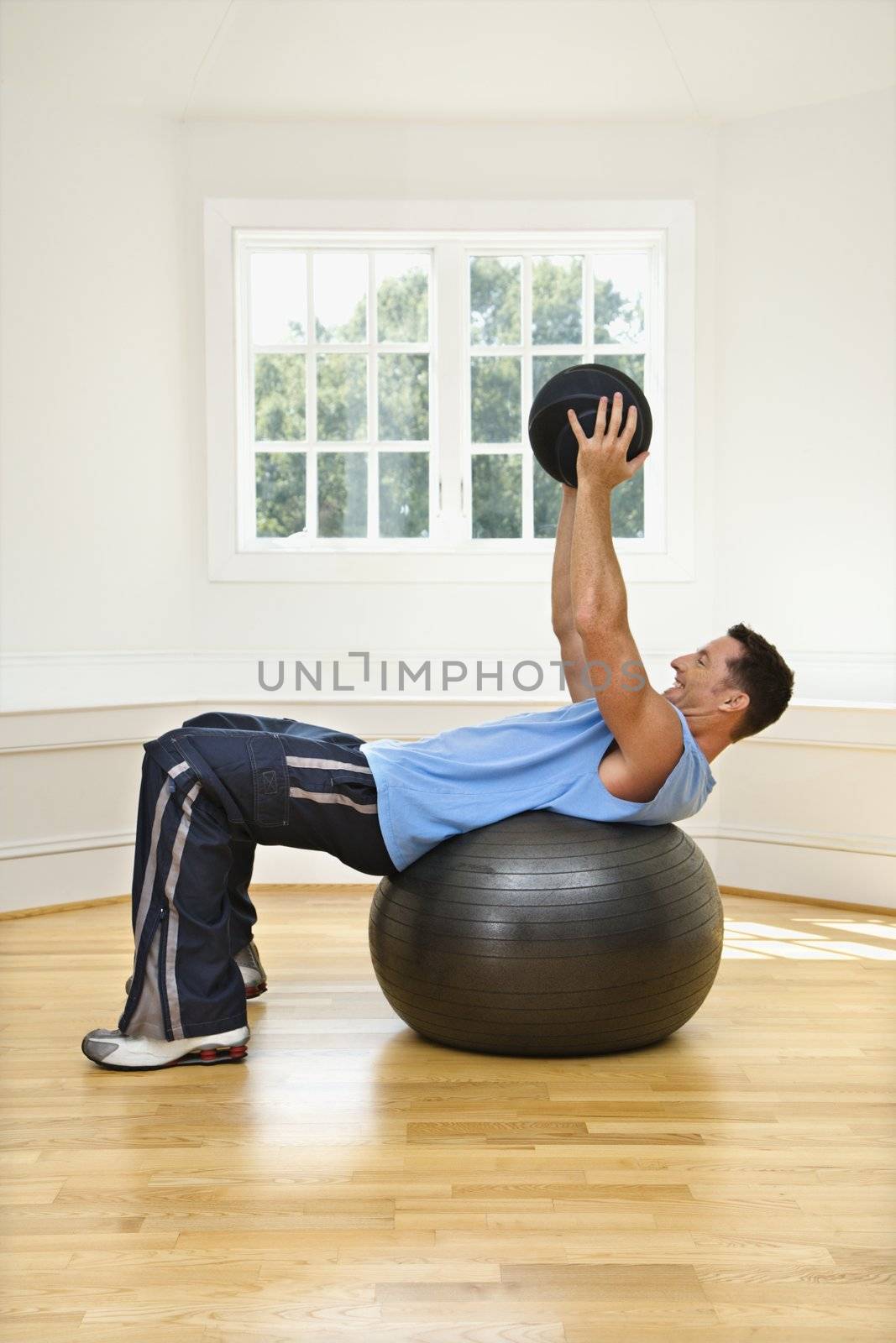 Man lifting medicine ball while on balance ball.