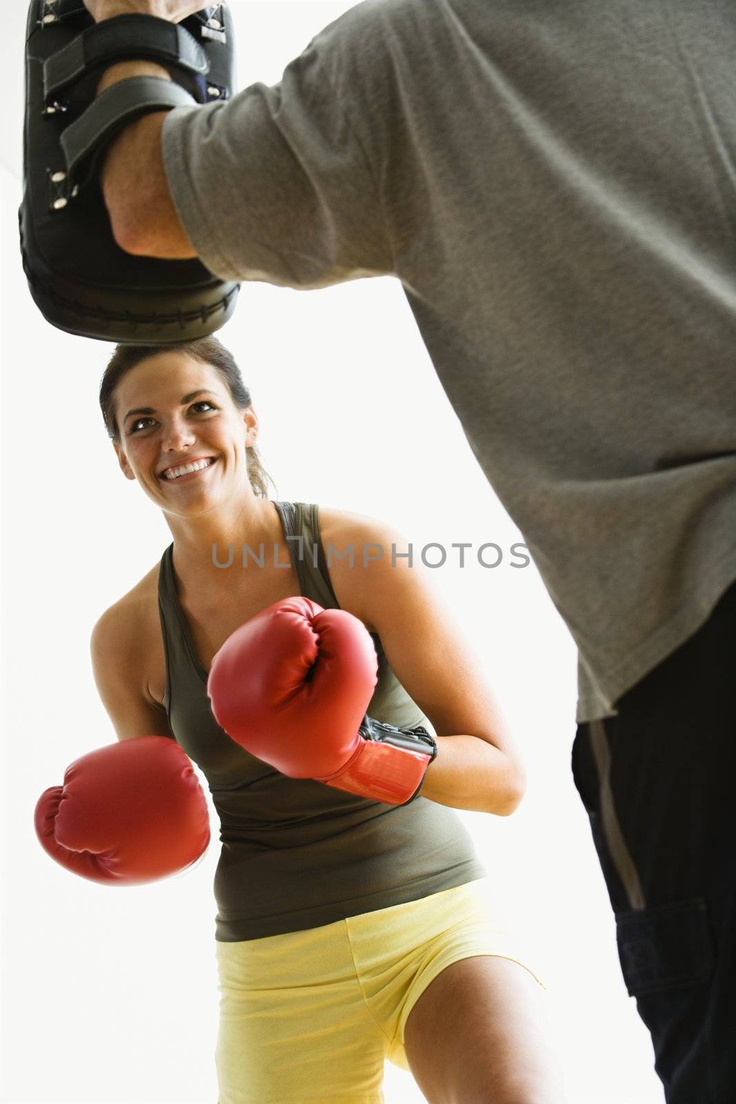 Woman wearing boxing gloves hitting training mits man is holding.