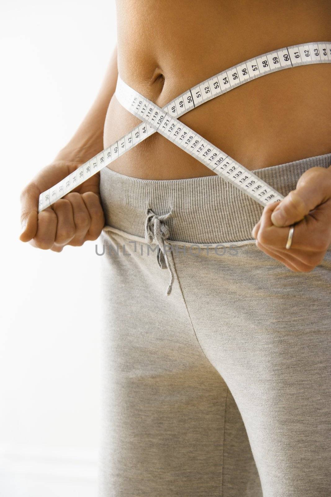 Woman standing pulling measuring tape around waist.