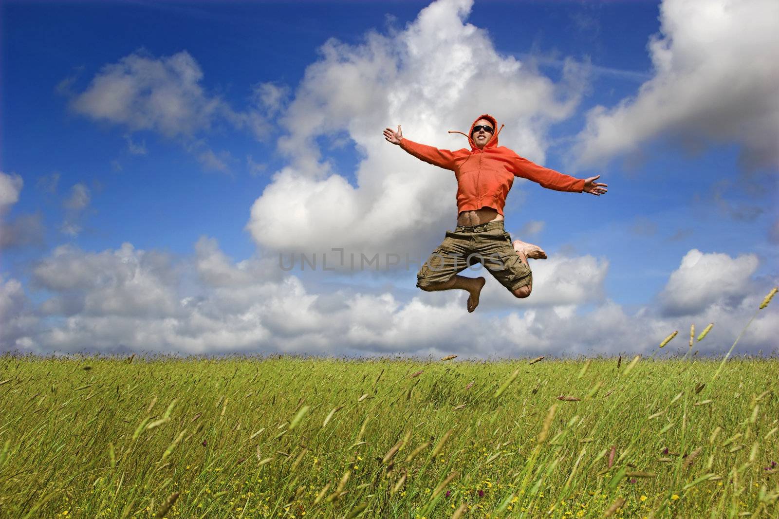 Man jumping on a green meadow with a beautiful cloudy sky