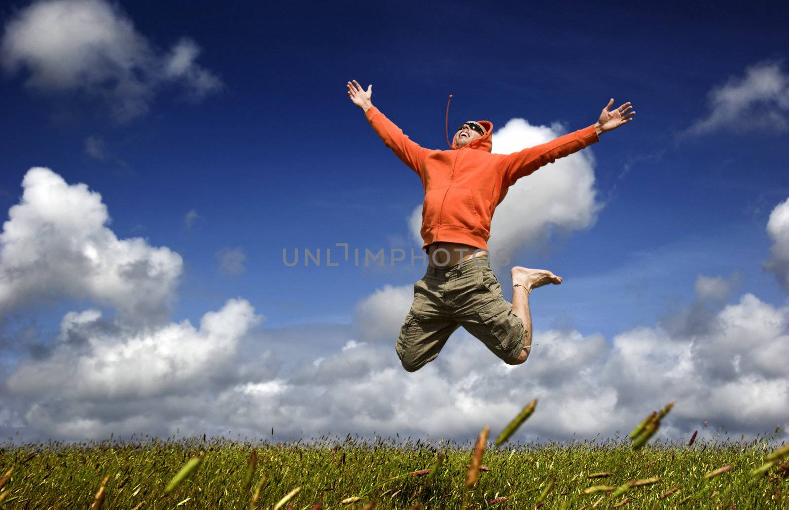 Man jumping on a green meadow with a beautiful cloudy sky