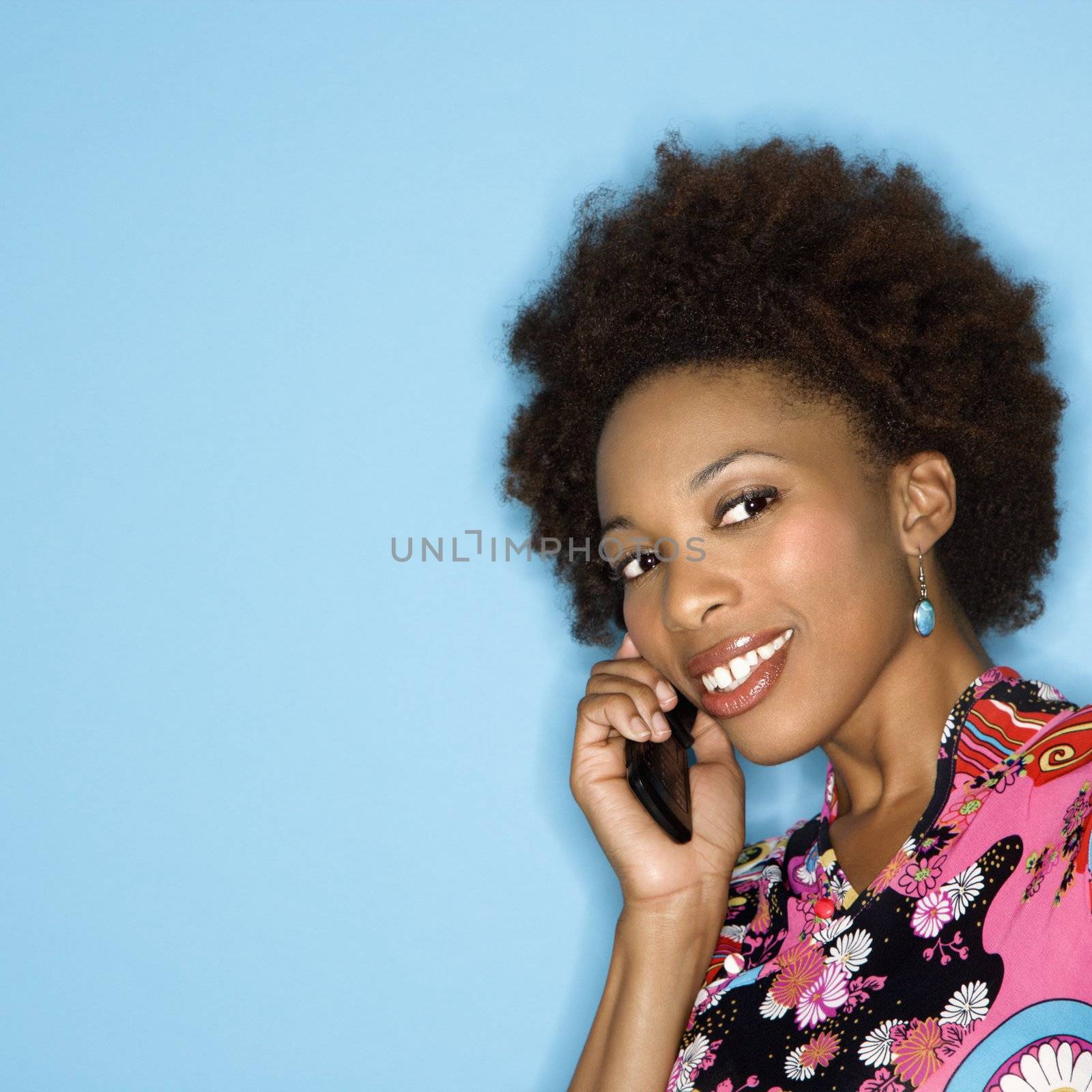 Woman with afro wearing vintage print fabric smiling holding cellphone.