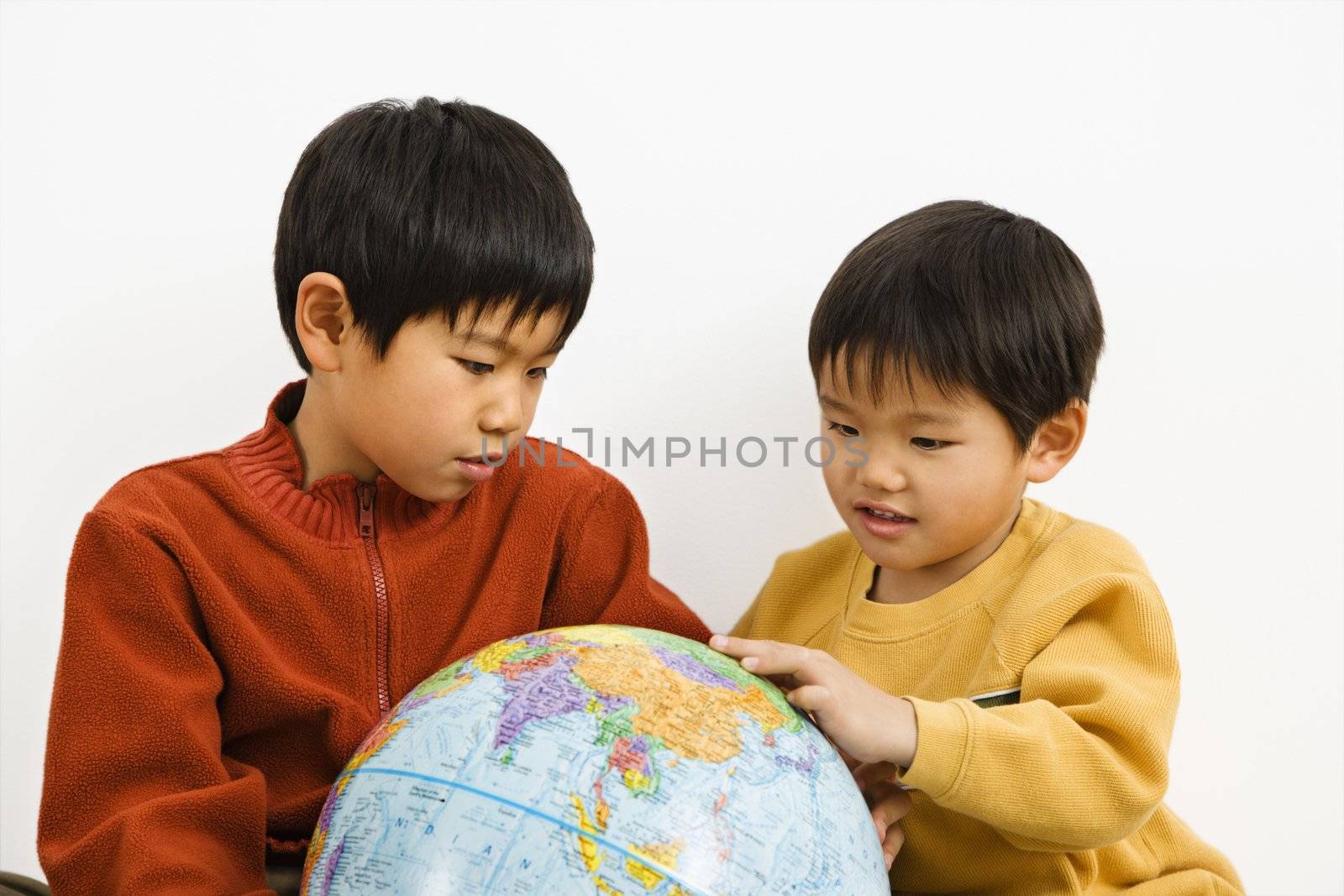 Two Asian boys looking and pointing at world globe