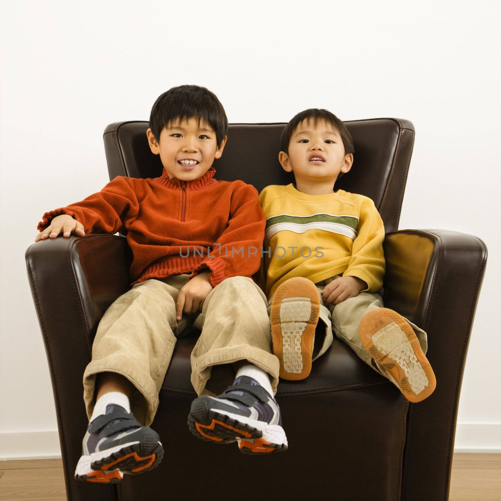 Two Asian brothers sitting in chair smiling.