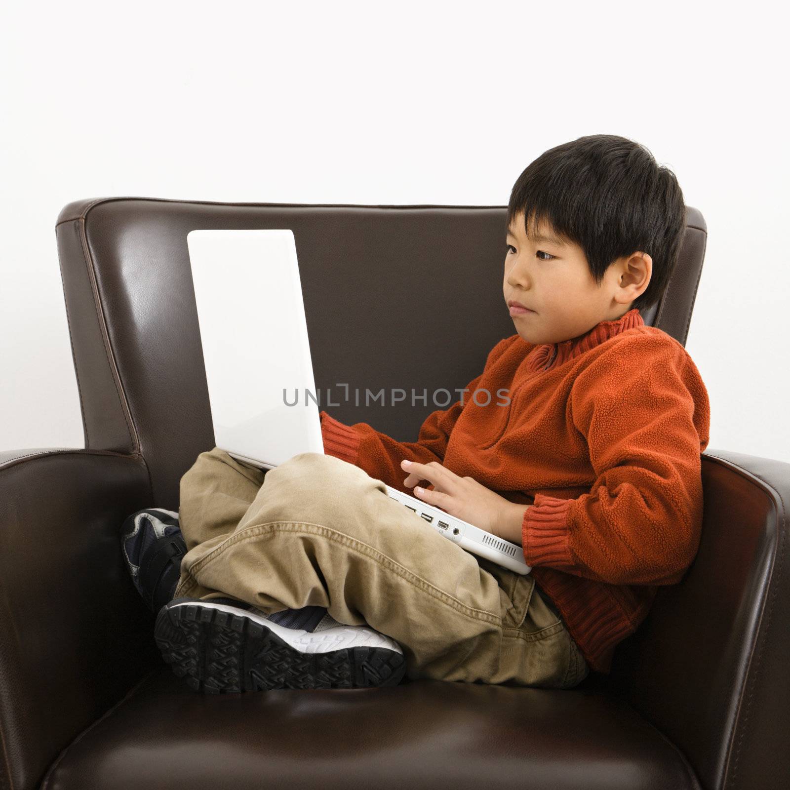 Asian boy with laptop computer sitting in chair.