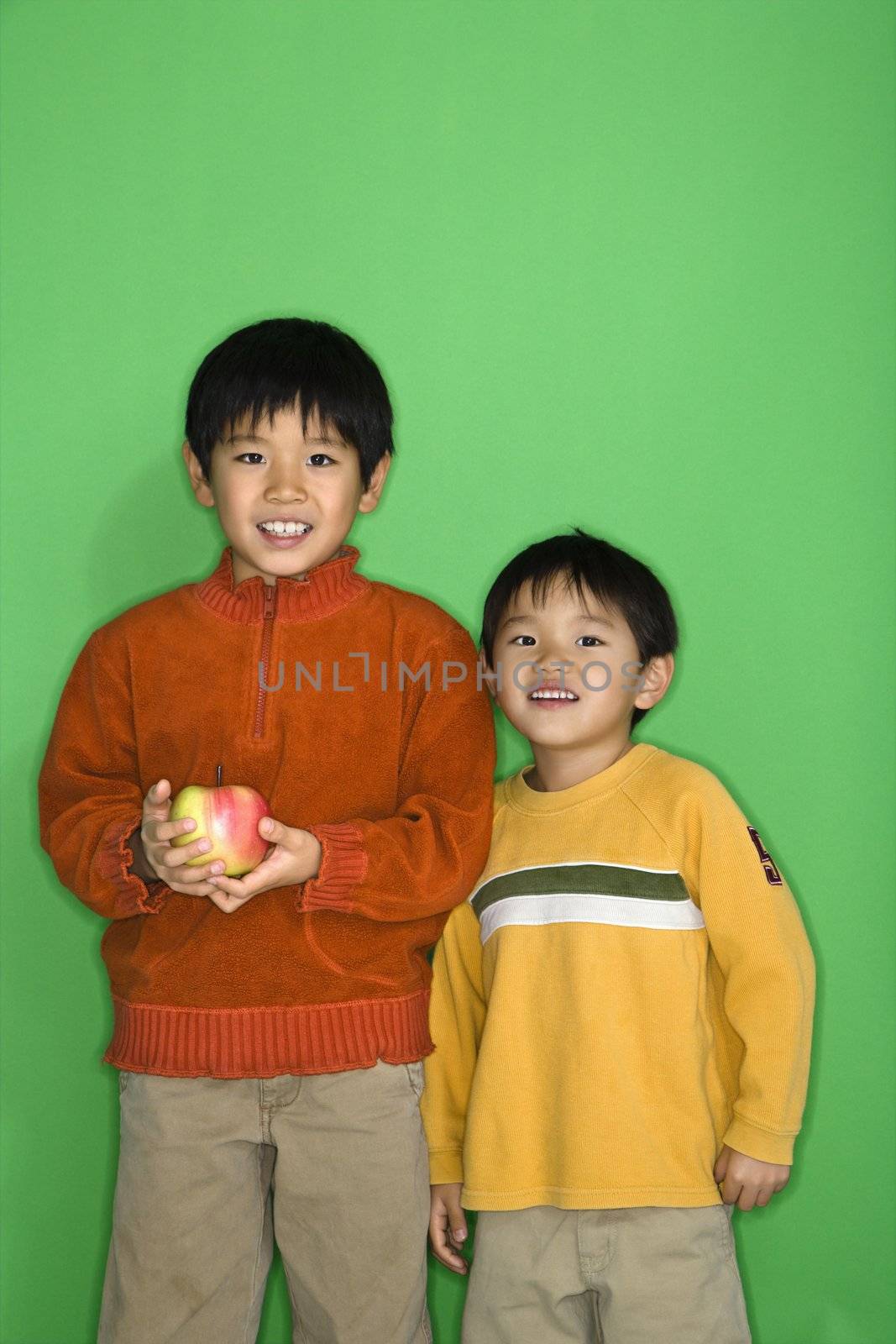 Two Asian boys holding apple smiling.