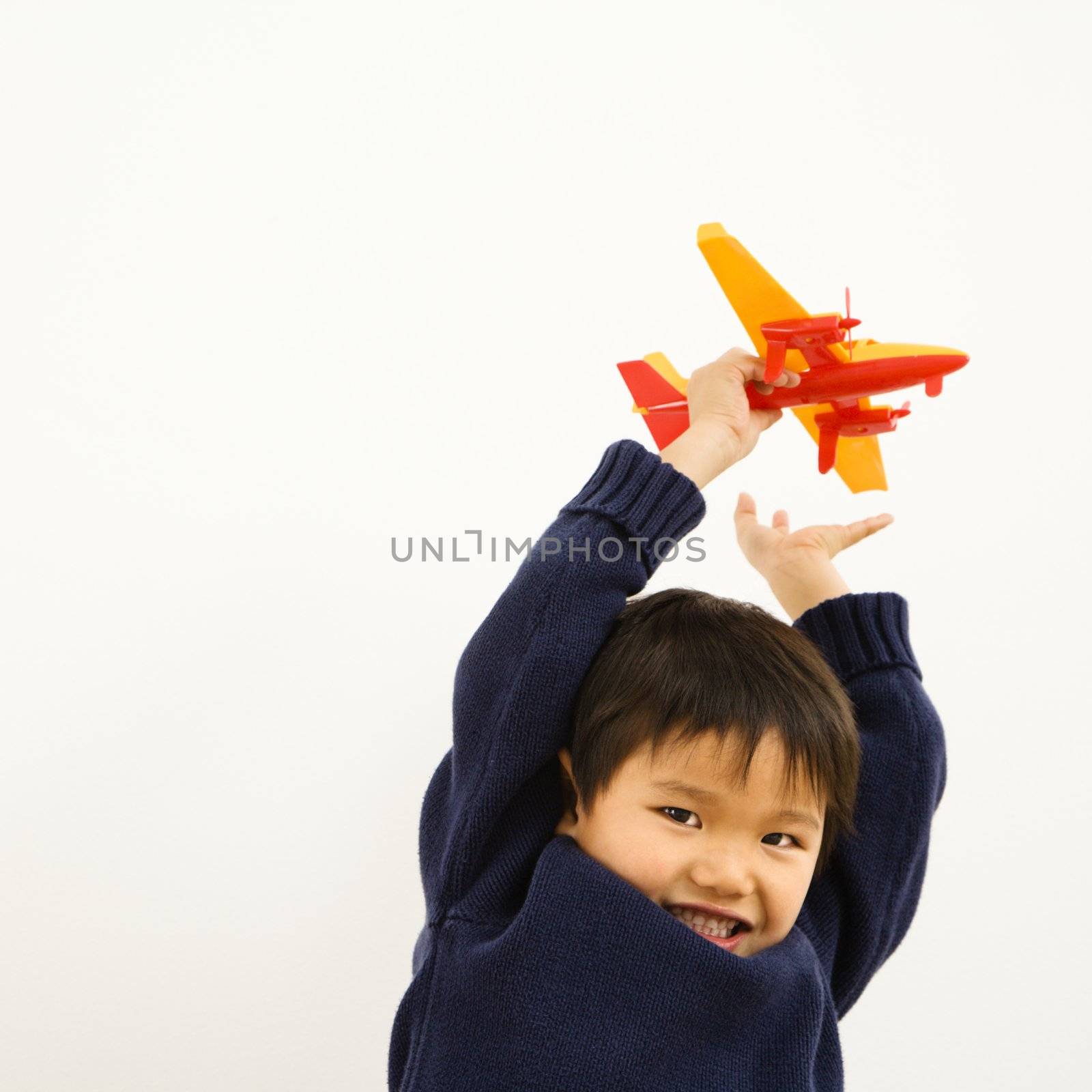 Young Asian boy playing with plastic toy airplane.