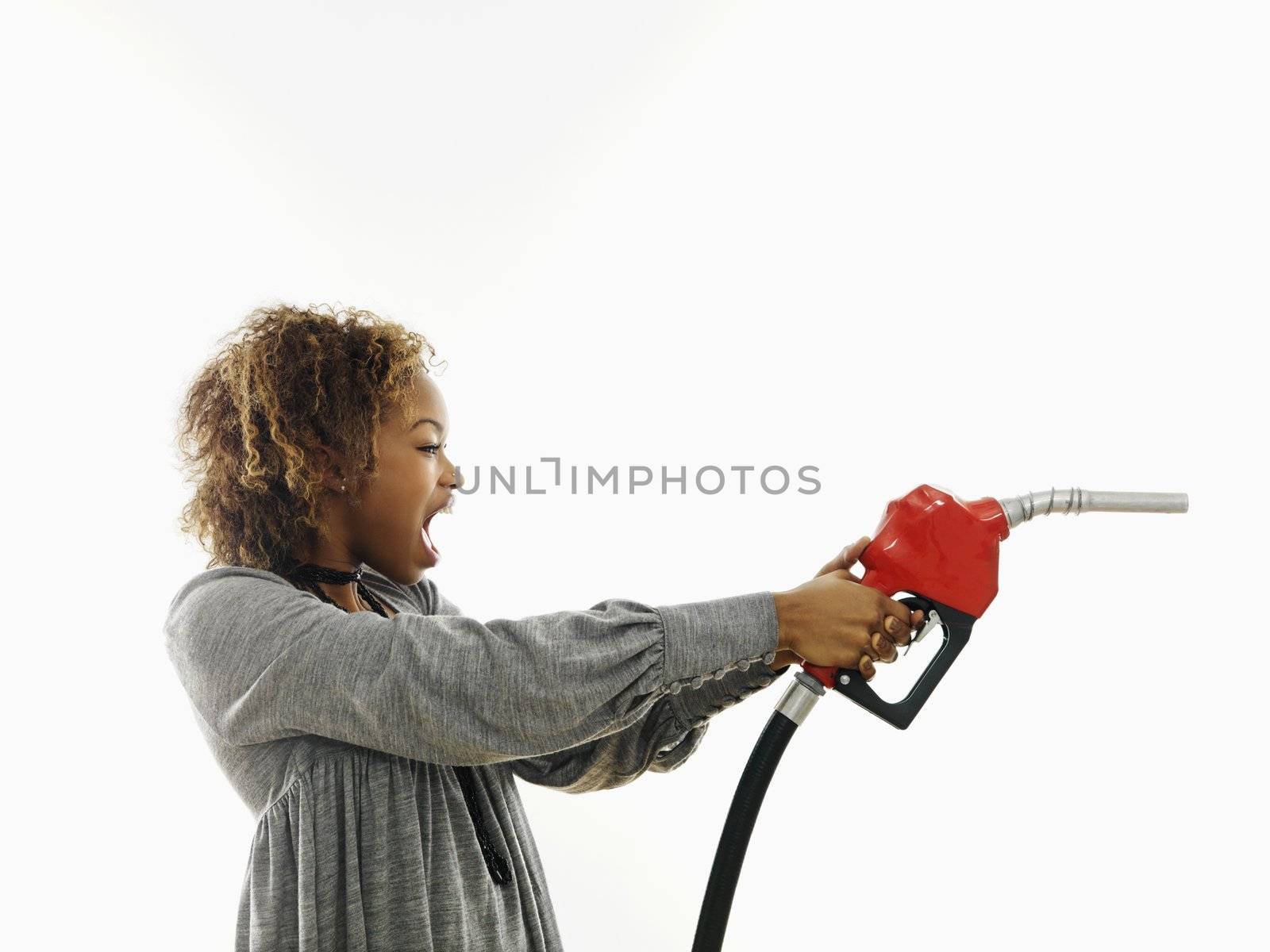 Portrait of pretty young woman holding gas pump nozzle like a gun making angry facial expression on white background.