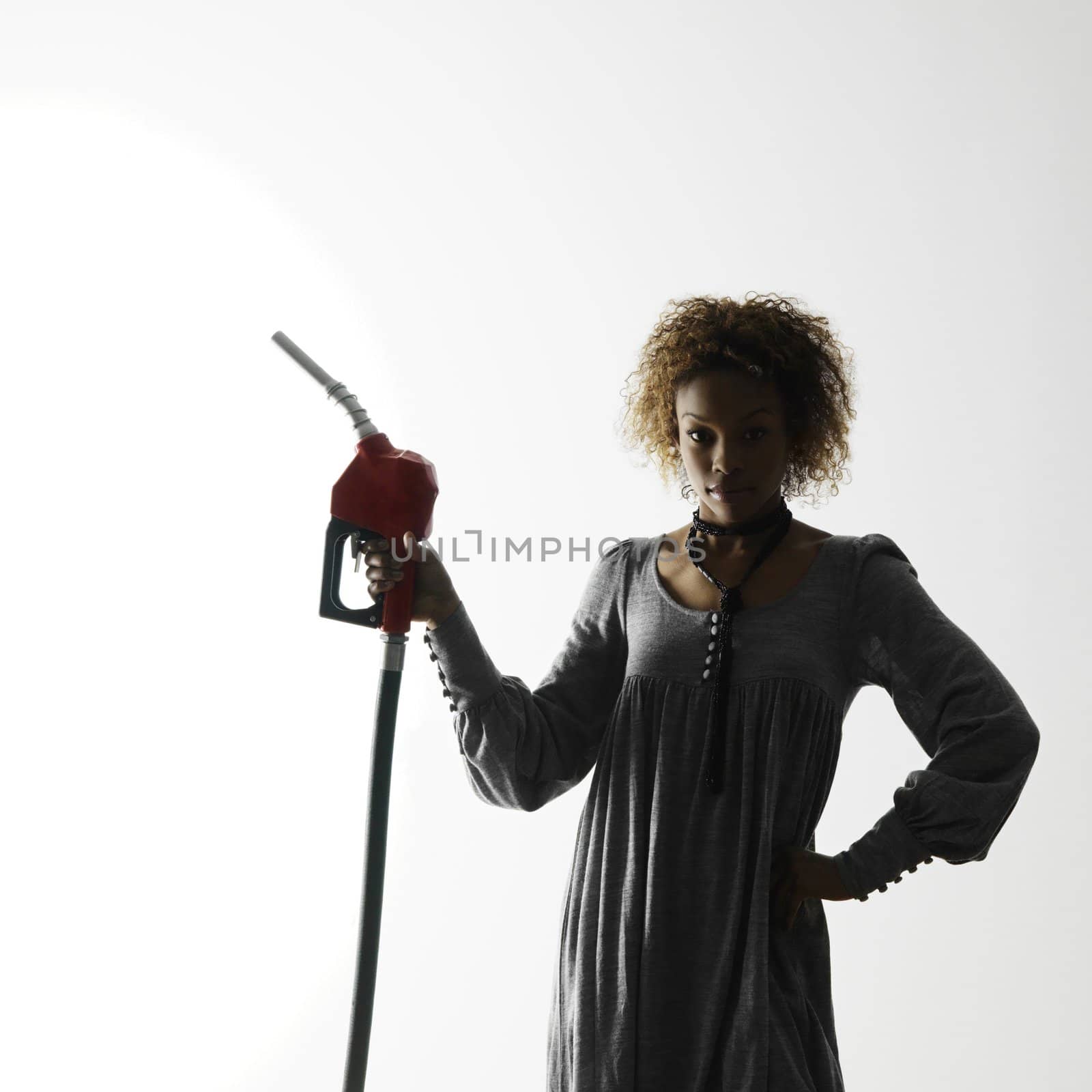 Woman holding gasoline pump nozzle against white background with dramatic studio lighting.