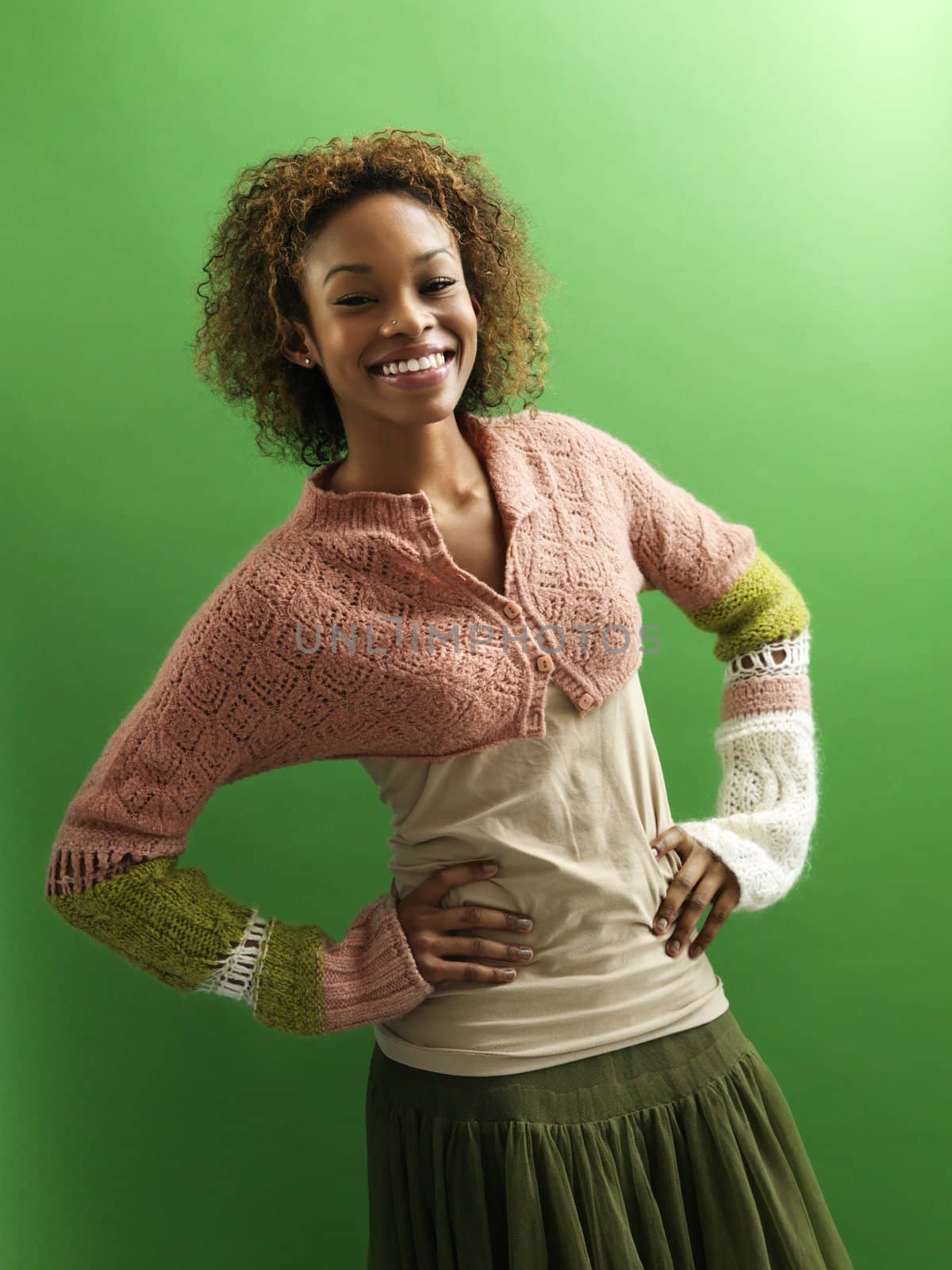Portrait of pretty young woman standing against green background with hands on hips smiling.