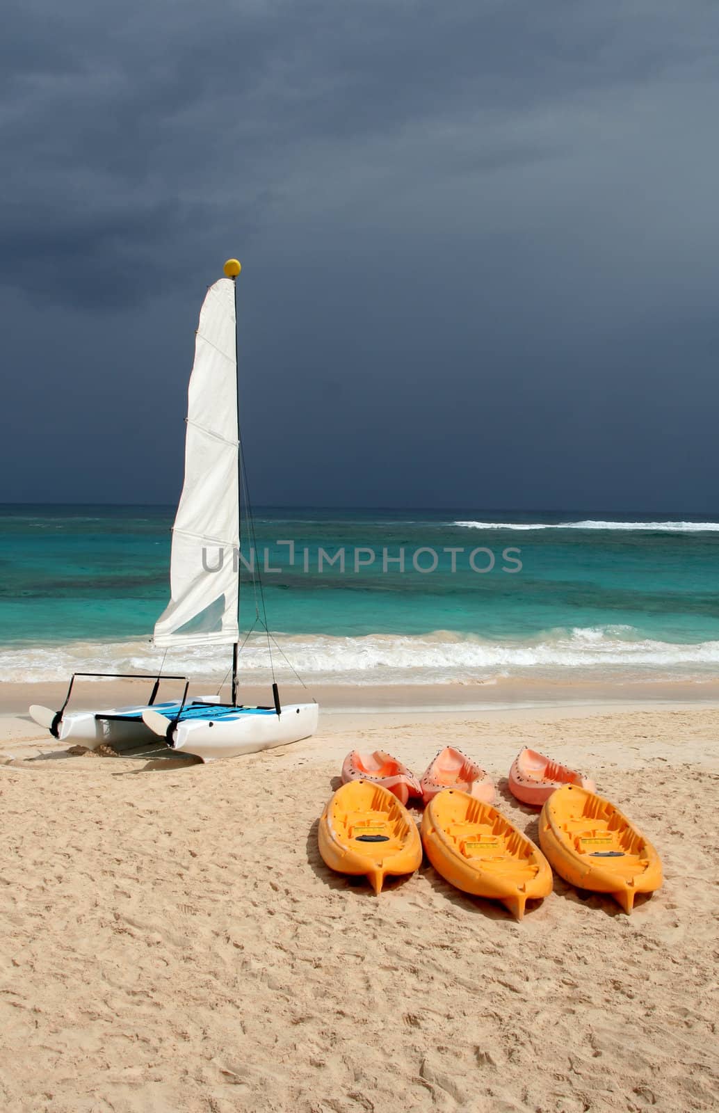 A catamaran and six plastic canoes sitting on shore at the beach.