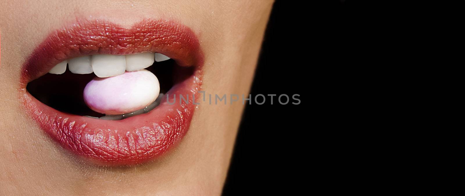 Detail of luscious female lips with candy clenched in teeth