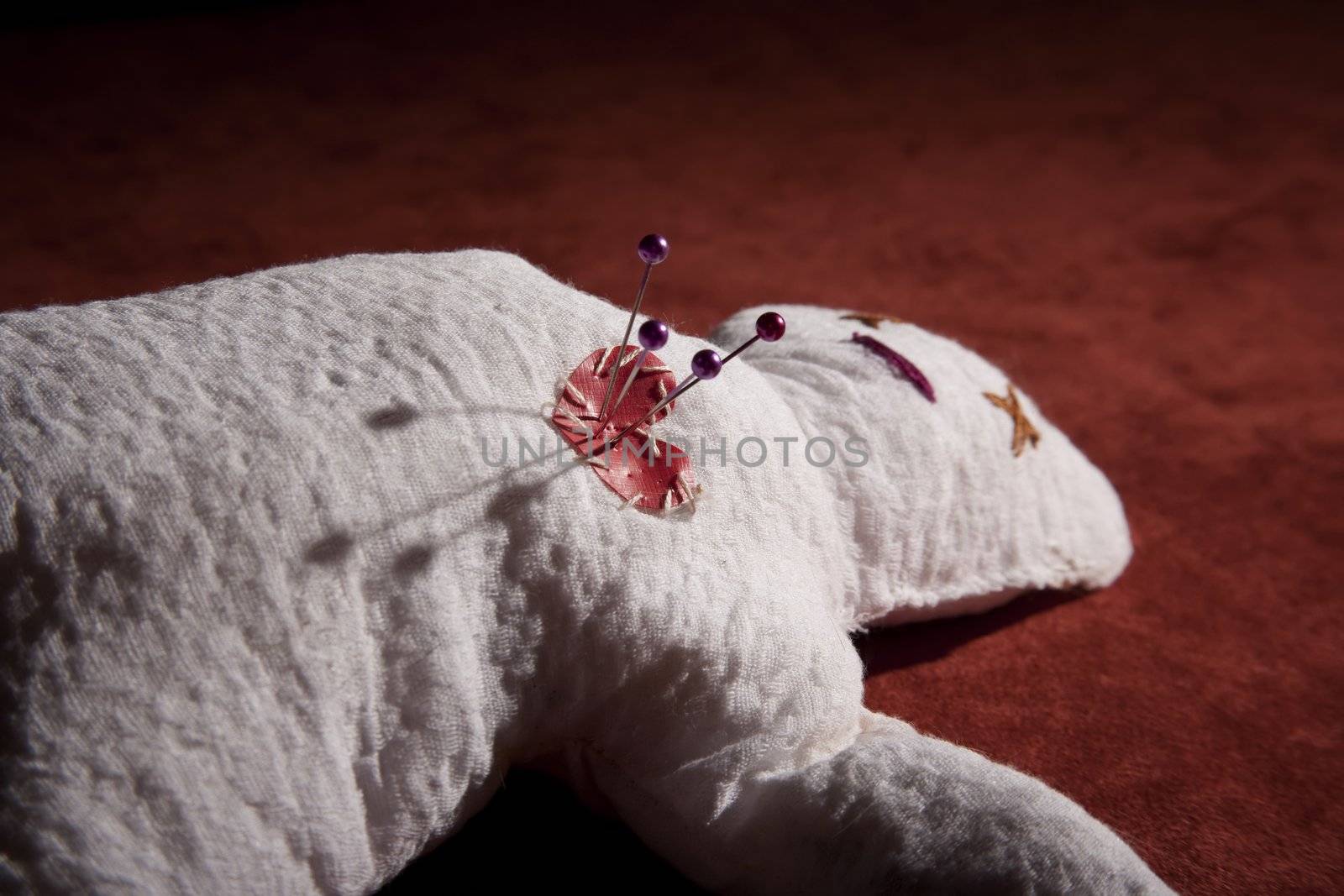 White Voodoo Doll with Pins in its Heart on Red Background
