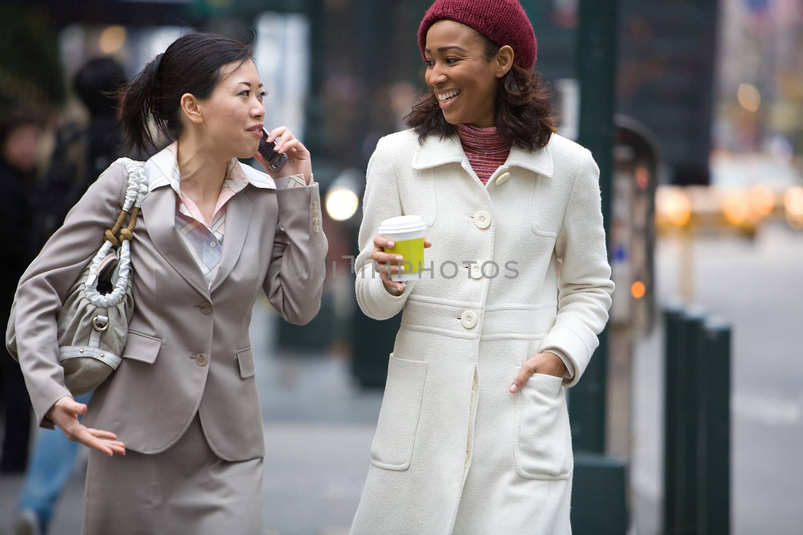 Two business women walking in the big city. One is on her cell phone.