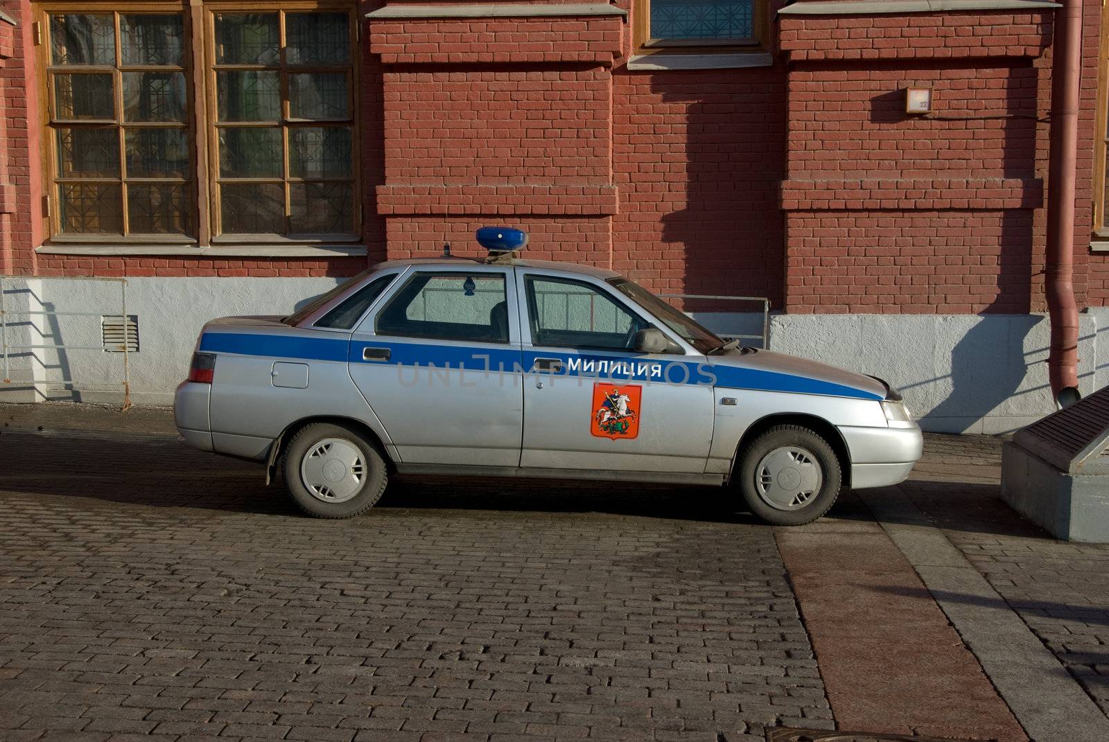 Police car on a cobblestone road near a building from a red brick