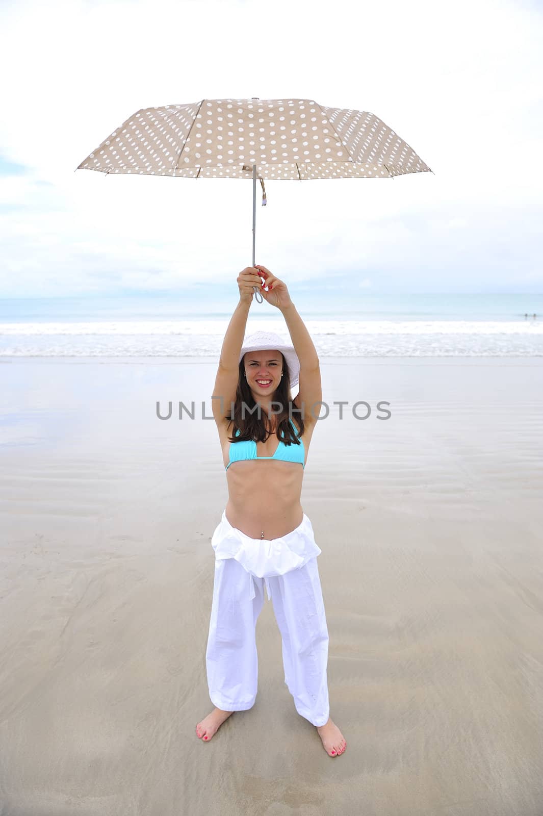 woman jumping on a tropical beach holding an umbrella 
