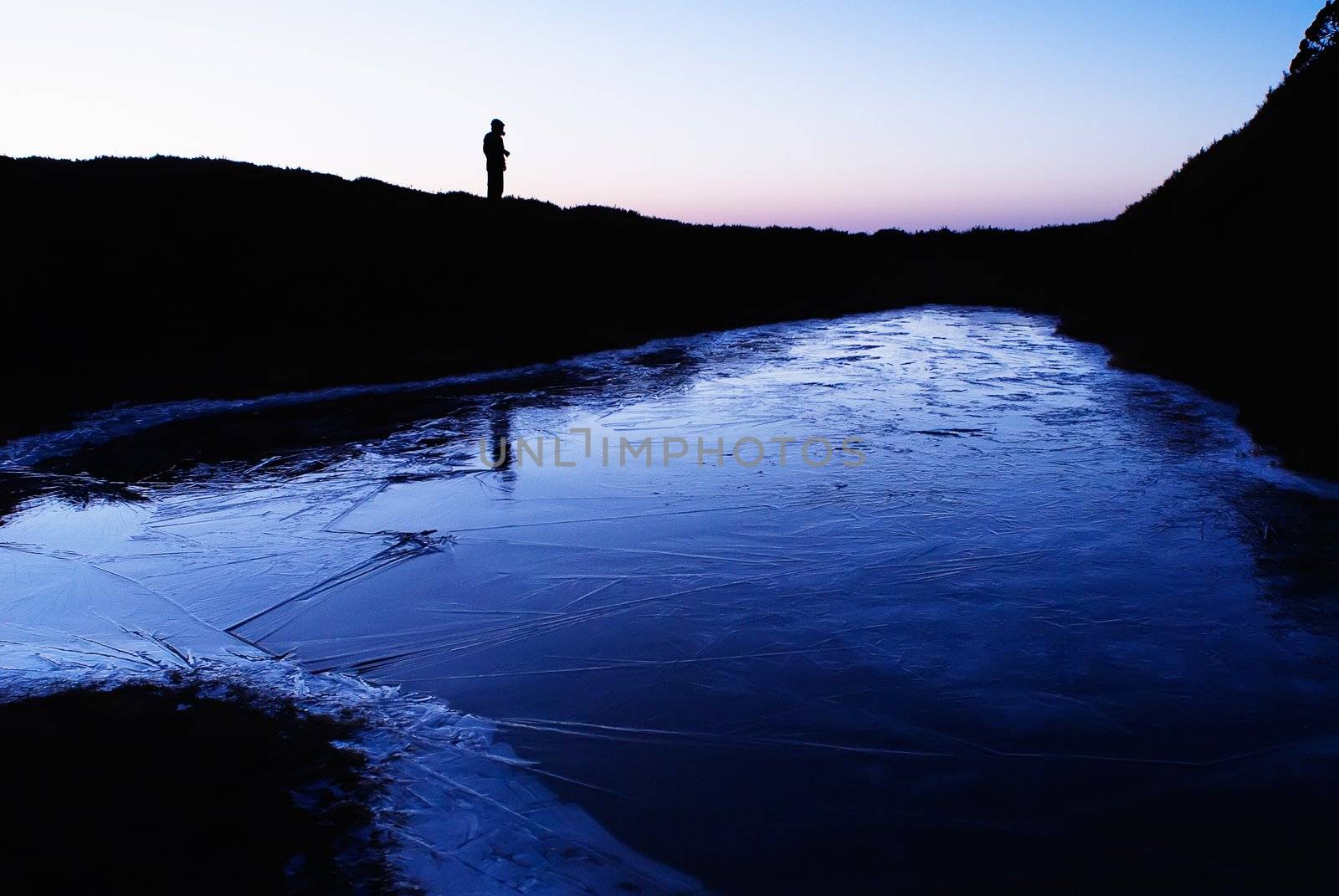 An iced lake with a man's silhouette in the morning.