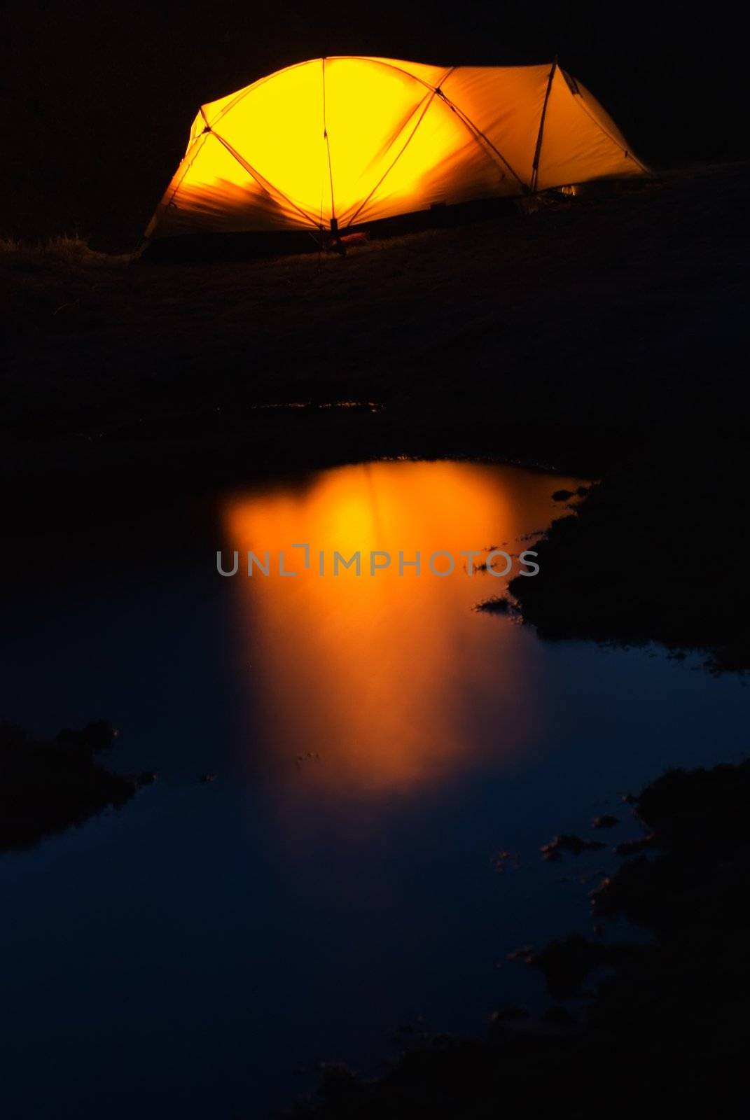 Tent in the night with weak light and small lake.