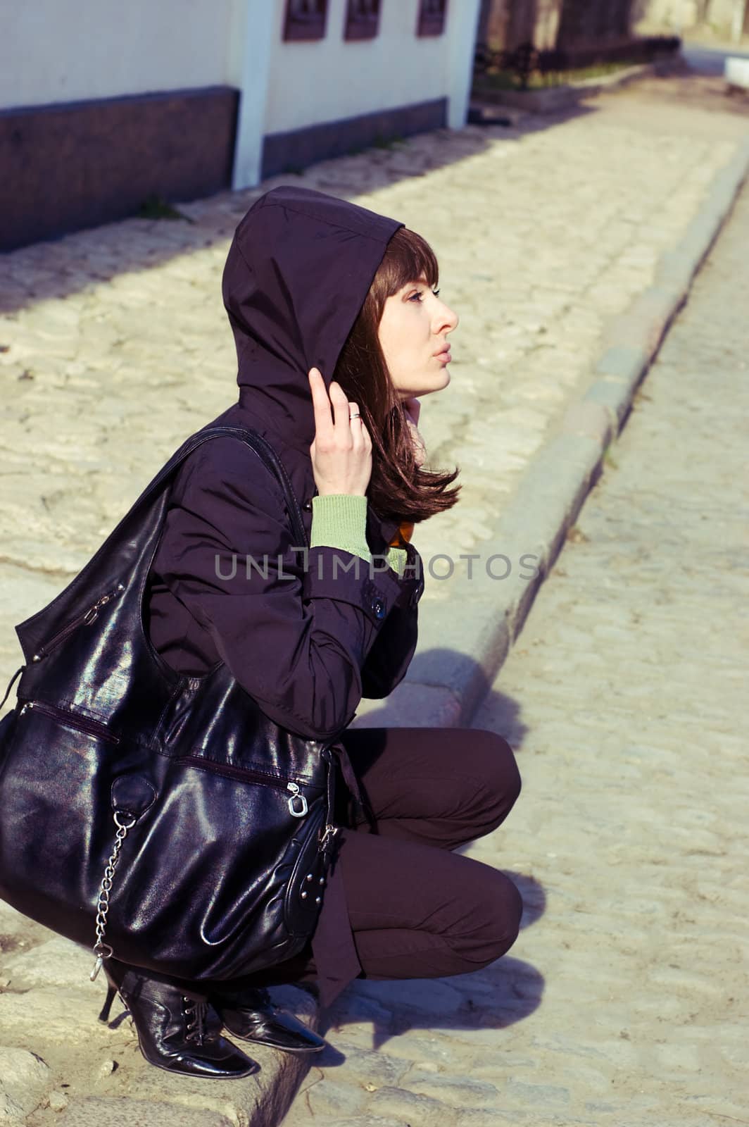 Sad brunette with hood on the pavement edge