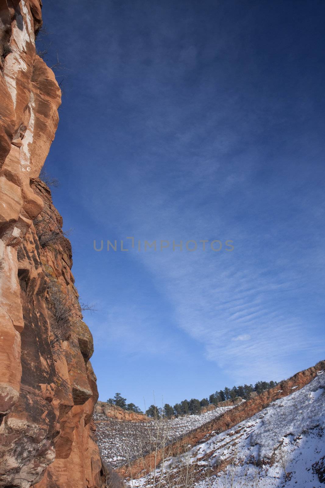 vertical red sandstone cliff framing blue sky in Colorado Rocky Mountains, winter scenery with snow