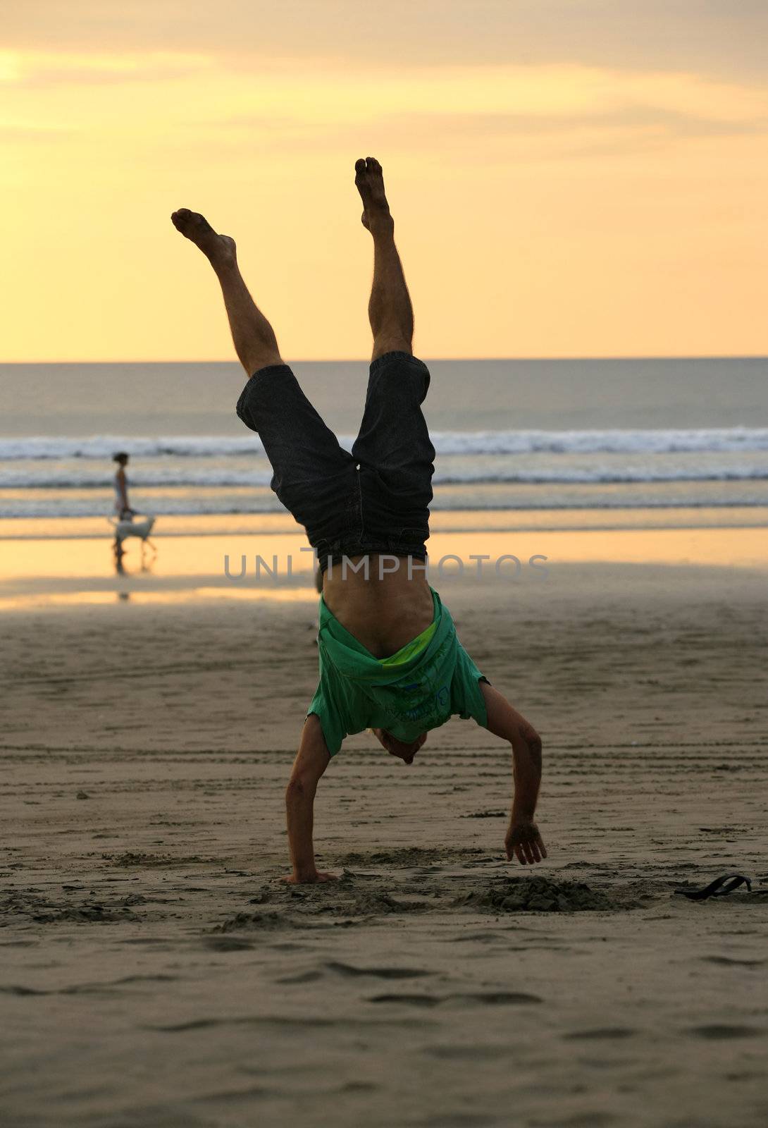 The man stands on hands on the beach by sunset