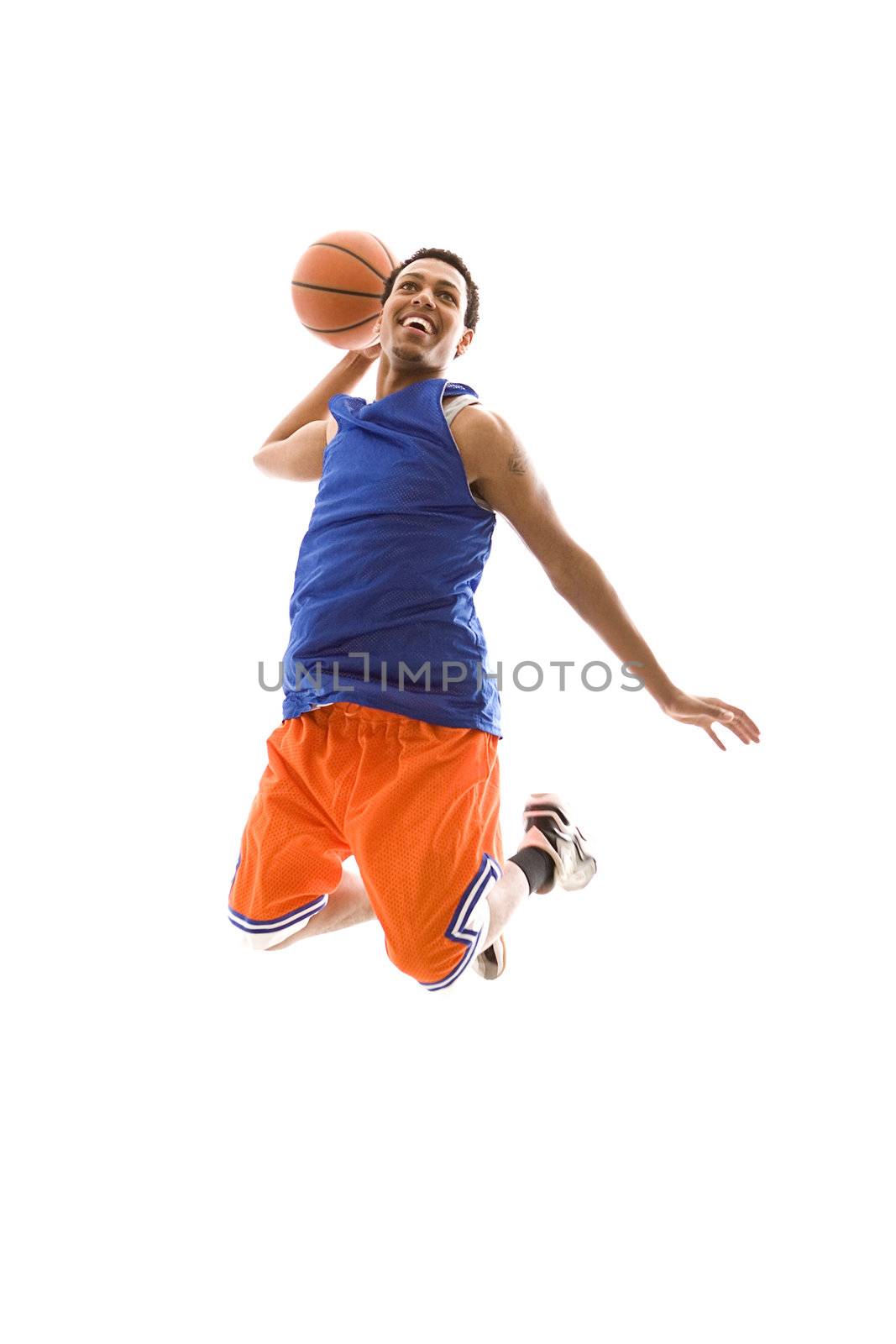 Young African American man playing basketball. It is a studio shot, and he is jumping in the air, about to slam dunk the basketball.