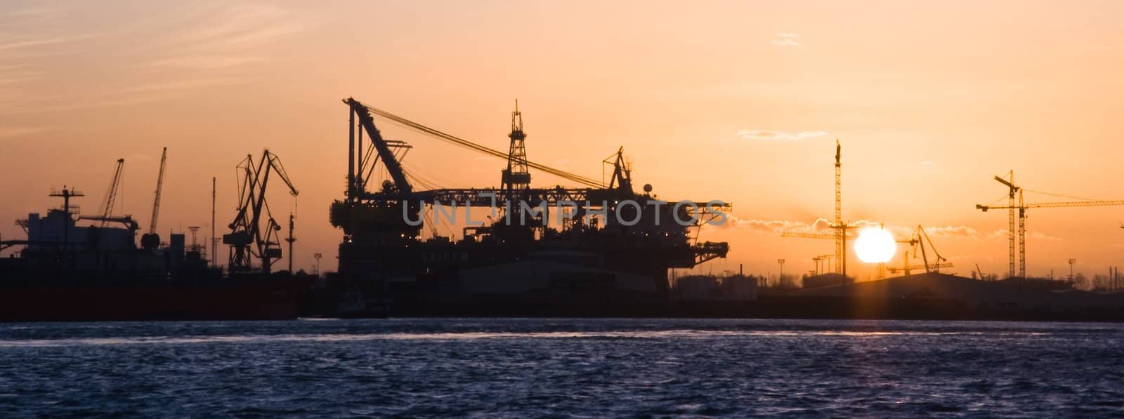 Silhouette of construction industry at the river with sinking sun on winter evening