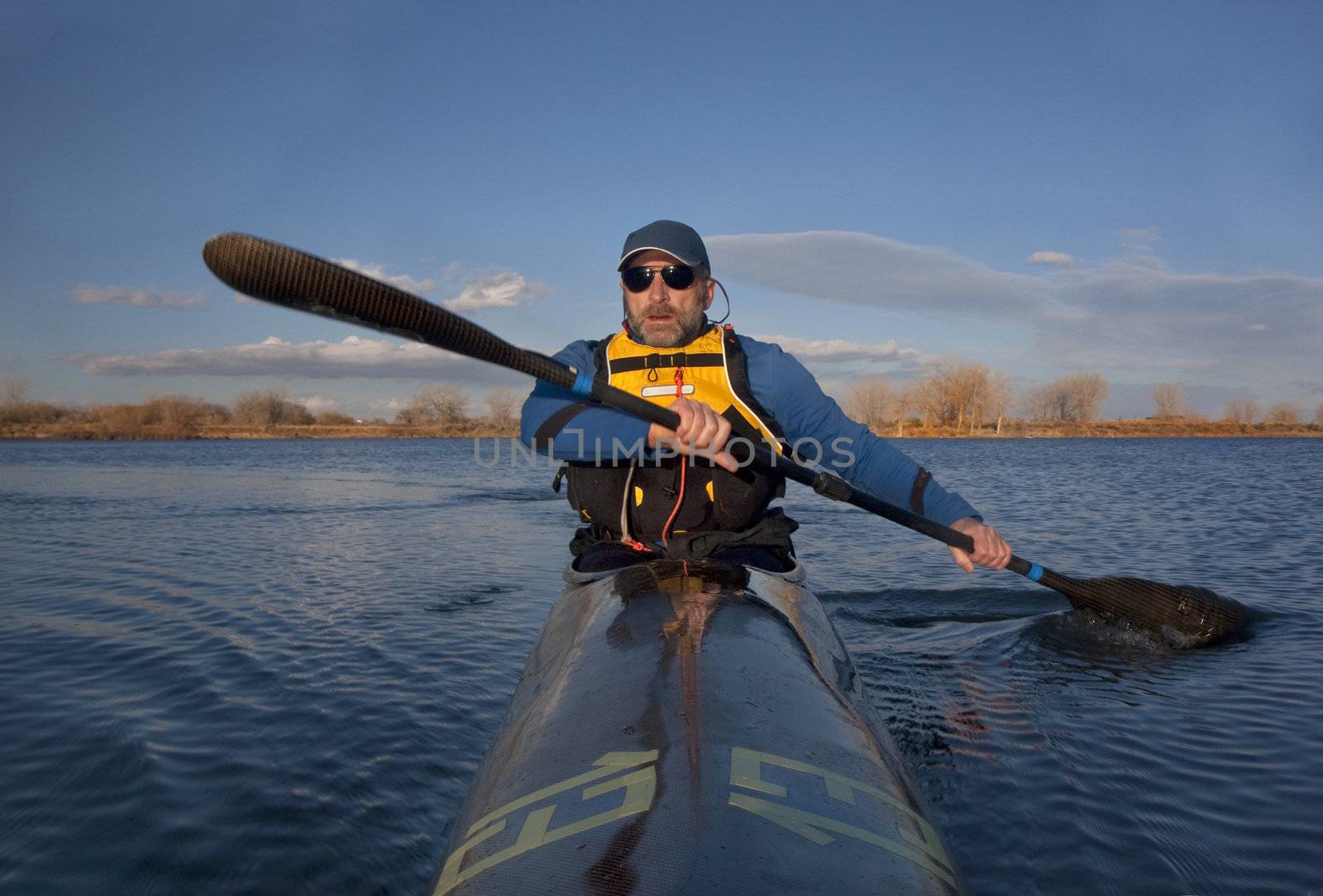 mature paddler exercising in a narrow carbon fiber racing kayak on a lake in early spring in Colorado, thirteen - temporary race number placed on deck by myself